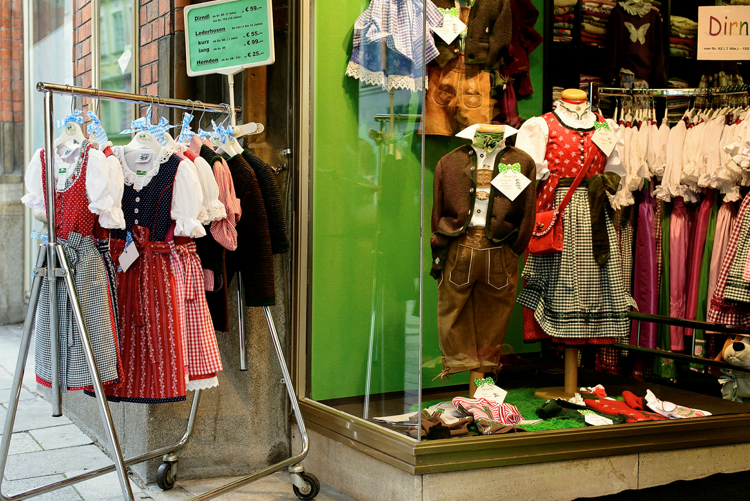 Ett skyltfönster med traditionella folkdräkter samt en klädställning utanför fylld med dirndl-klänningar. (AI-genererad text)