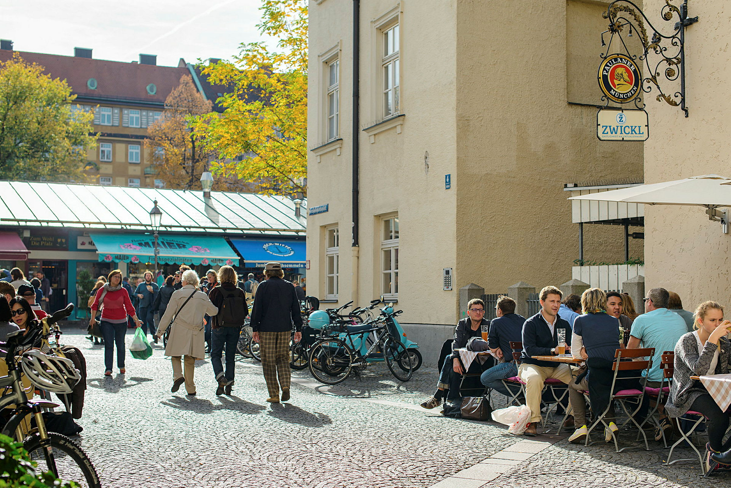 Ett torg med människor, cyklar och ett café med uteservering. (AI-genererad text)