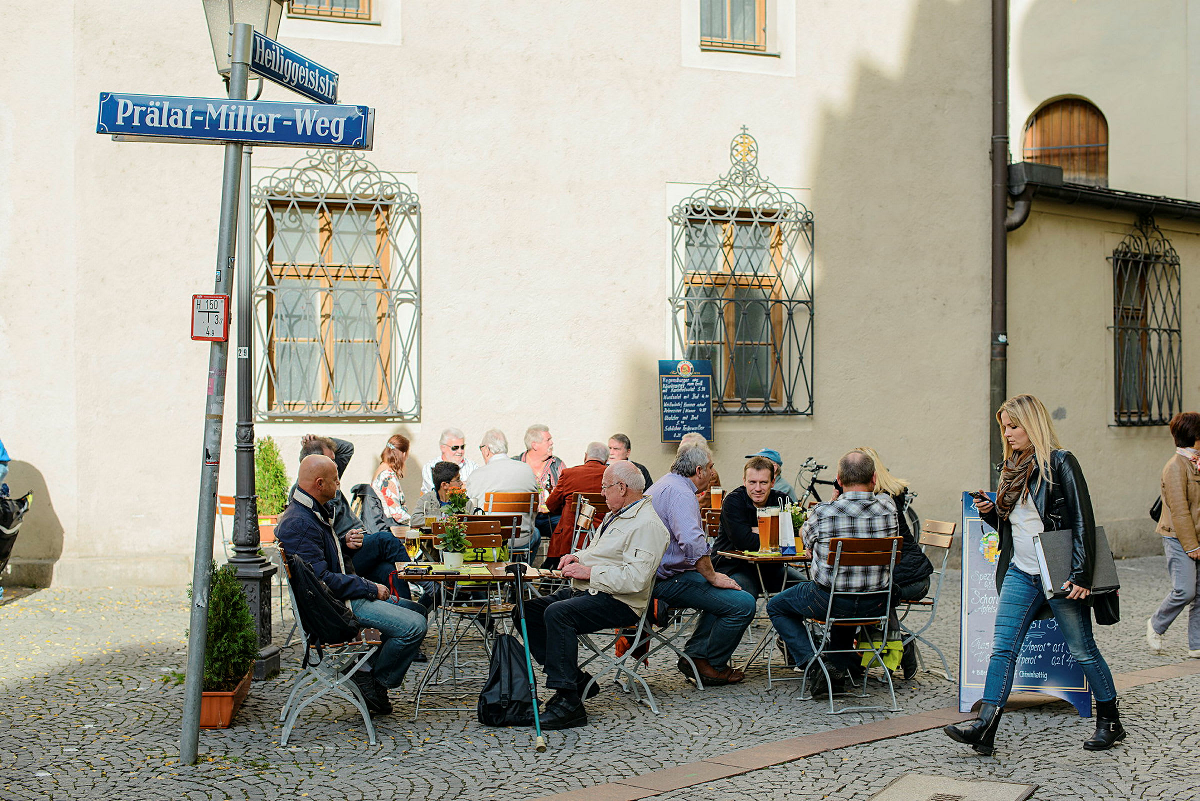 Personer njuter av mat och dryck vid cafébord utomhus på en kullerstensgata. (AI-genererad text)