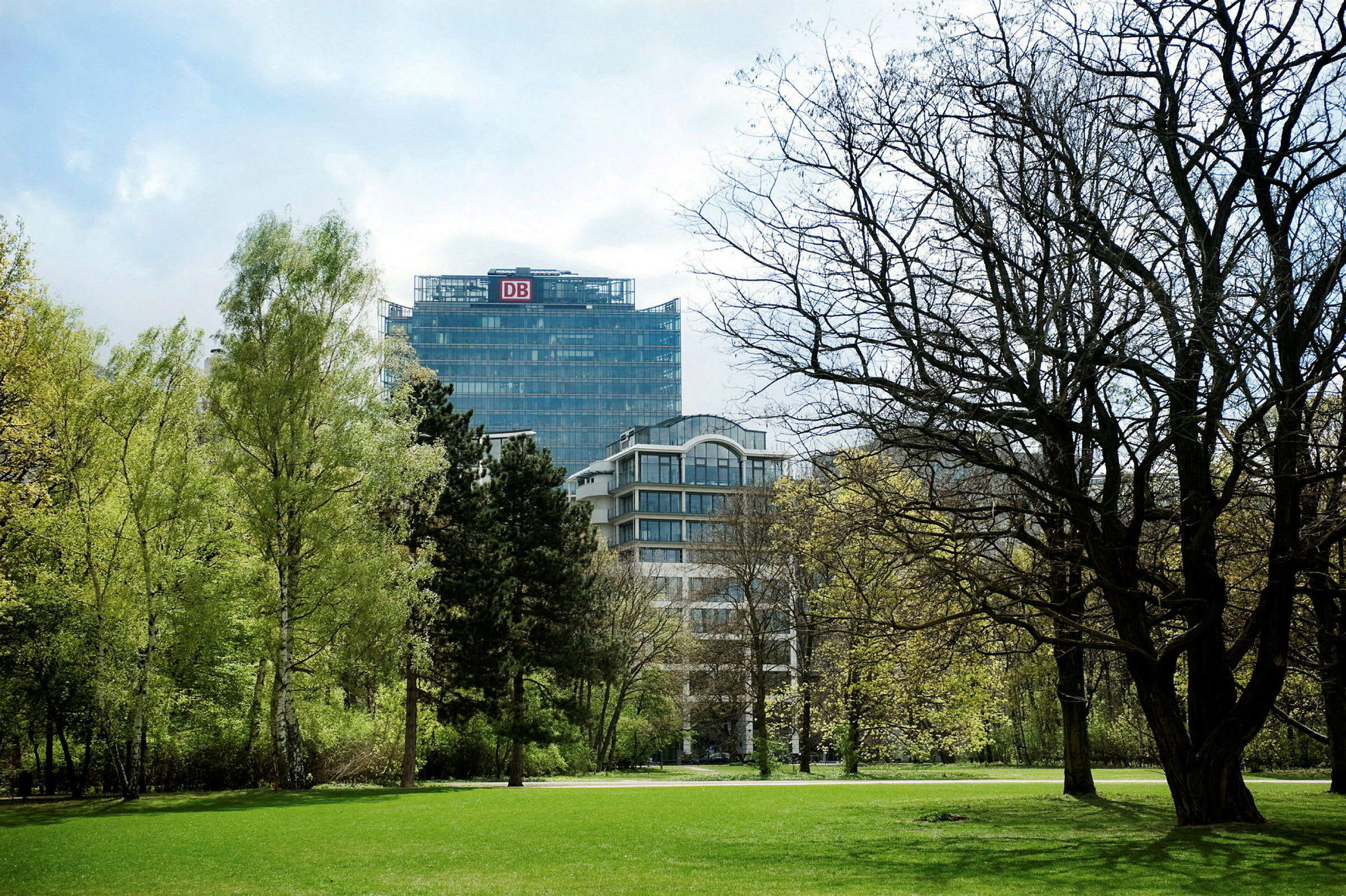Bild av en park med gröna träd och gräsmatta. I bakgrunden syns en modern kontorsbyggnad. (AI-genererad text)
