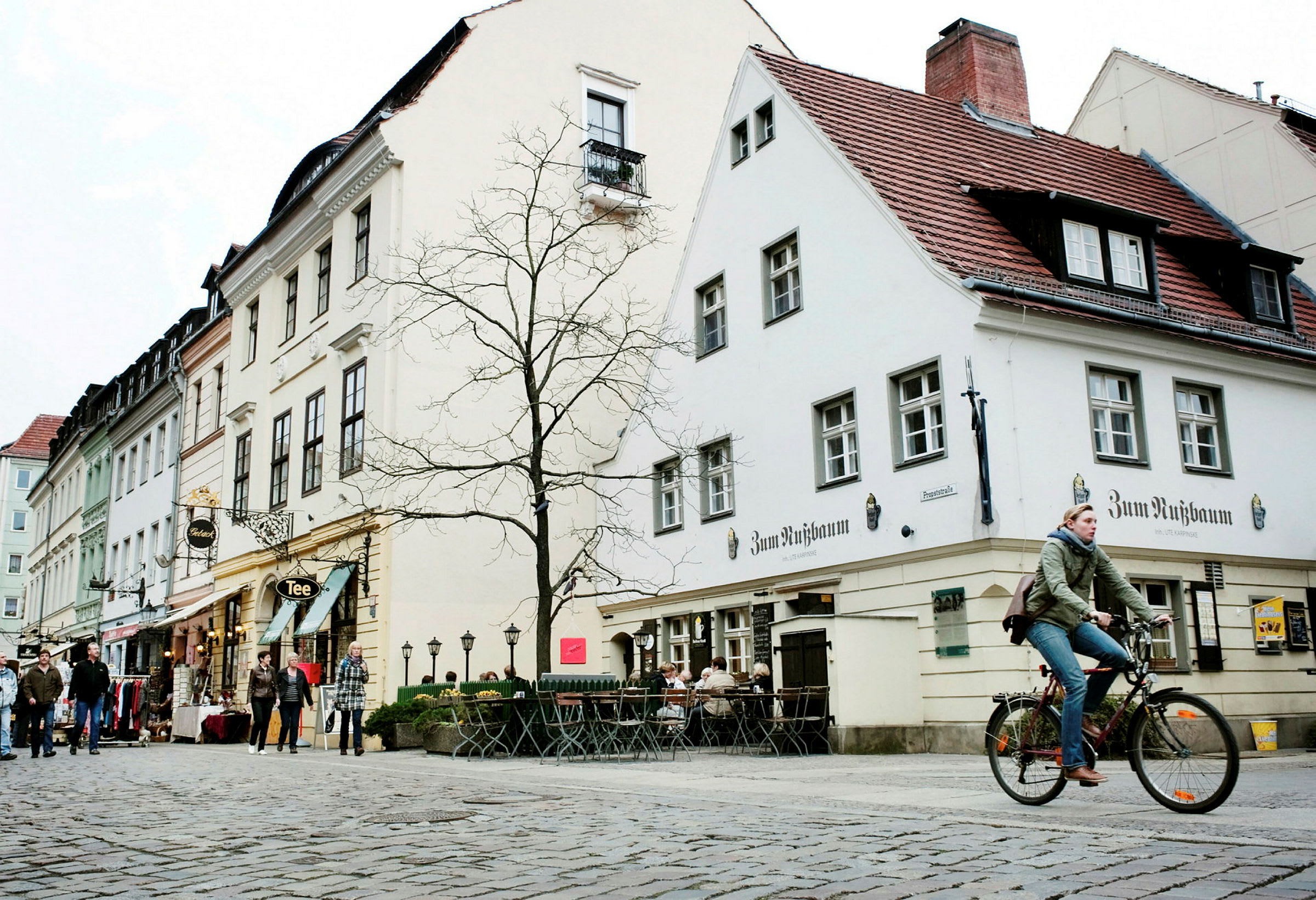 En gata med kullersten, omgiven av byggnader, en gående person och en person som cyklar. (AI-genererad text)