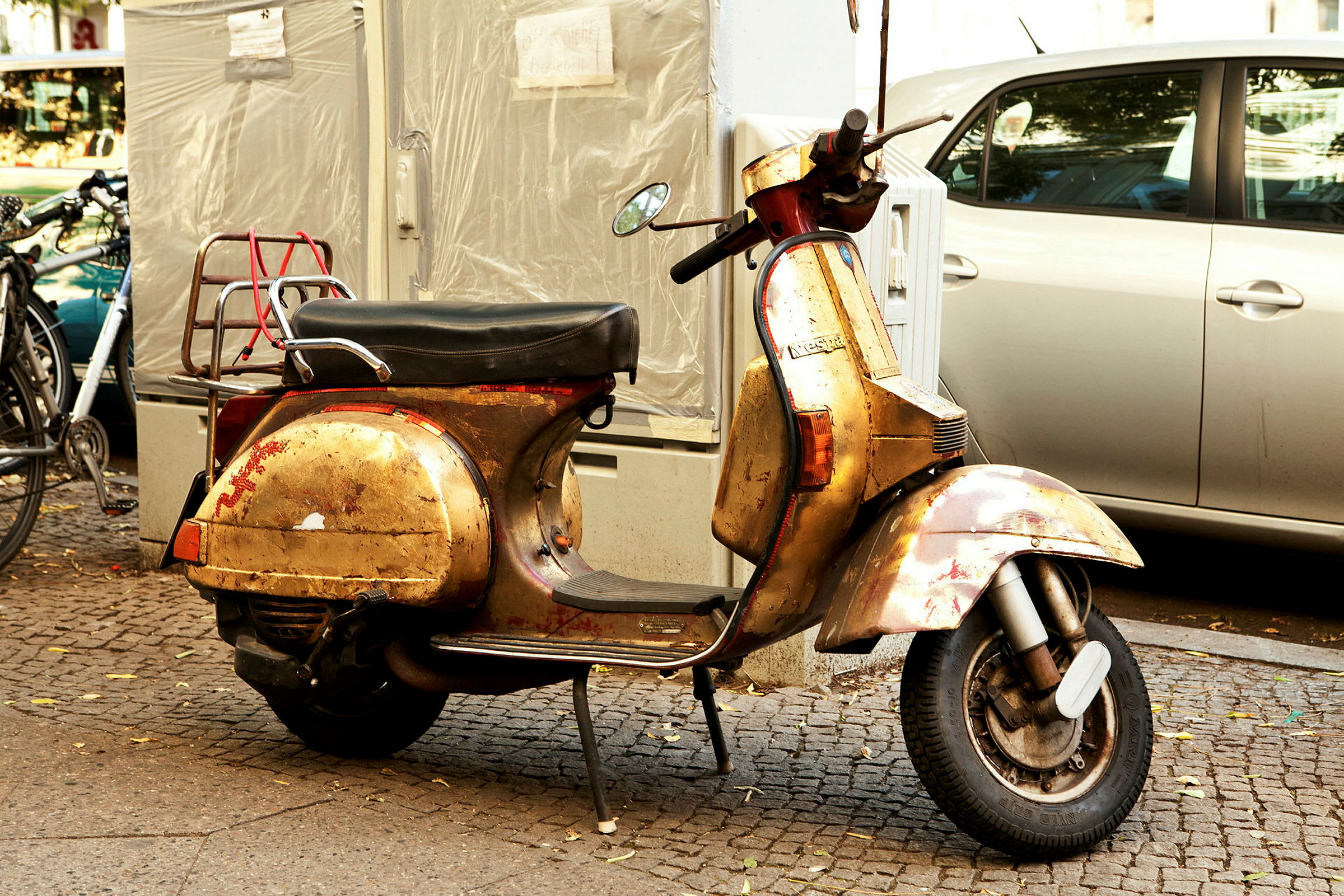 En gammal guldfärgad scooter står parkerad på en trottoar intill andra fordon. (AI-genererad text)