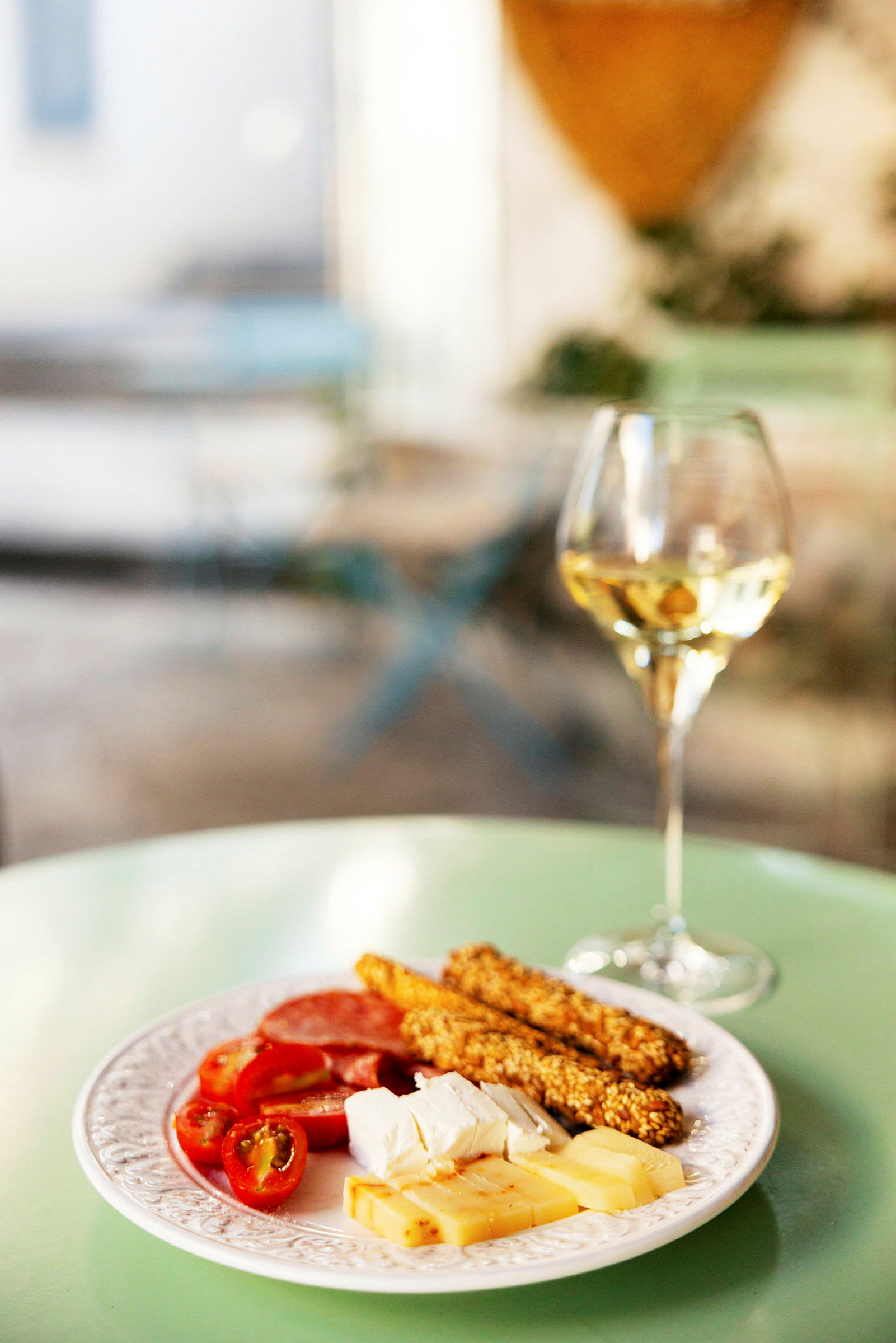 En tallrik med ost, brödsticks och körsbärstomater, bredvid ett glas vitt vin, placerat på ett grönt bord. (AI-genererad text)