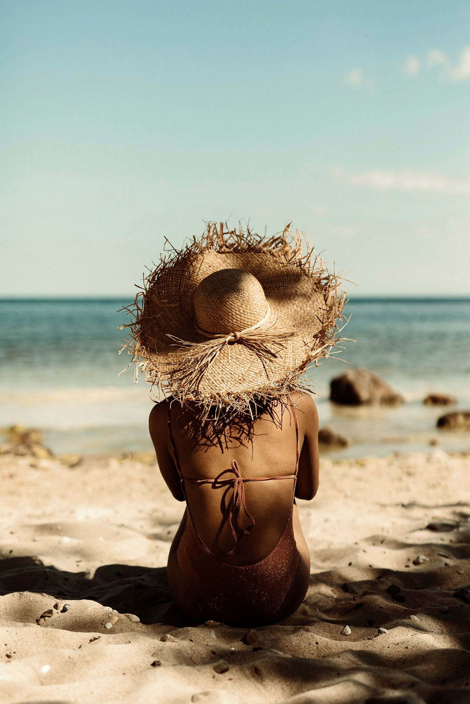 En person med solhatt sitter på stranden med havet i bakgrunden. (AI-genererad text)