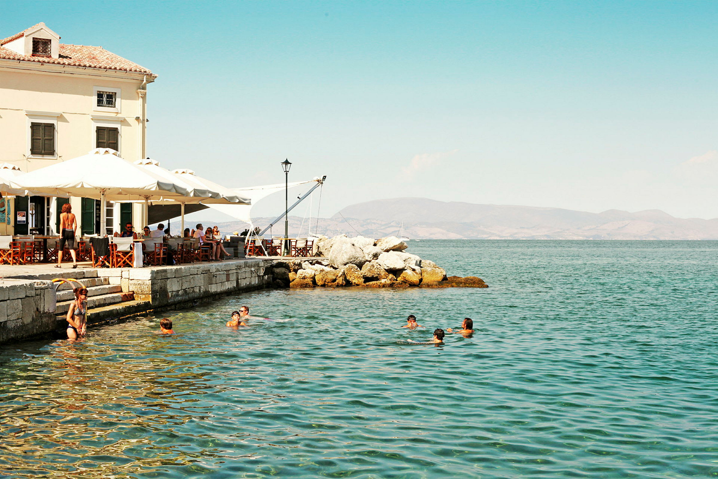 Personer simmar i havet nära ett café vid stranden. (AI-genererad text)