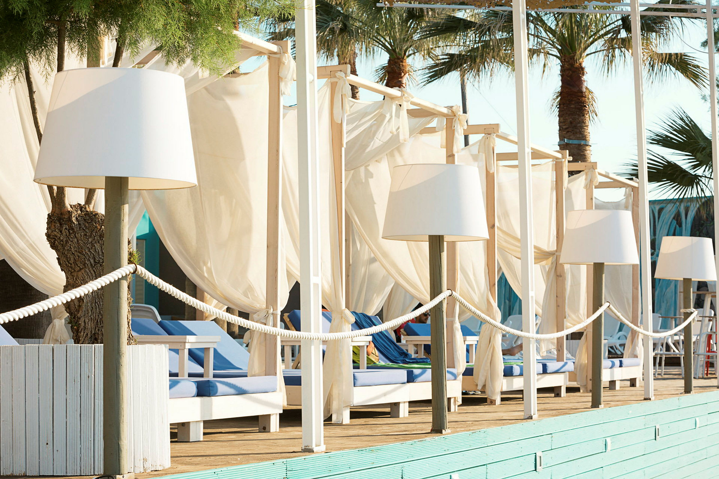 Rad av solstolar med vita tyger och lampor vid en pool eller strand. (AI-genererad text)