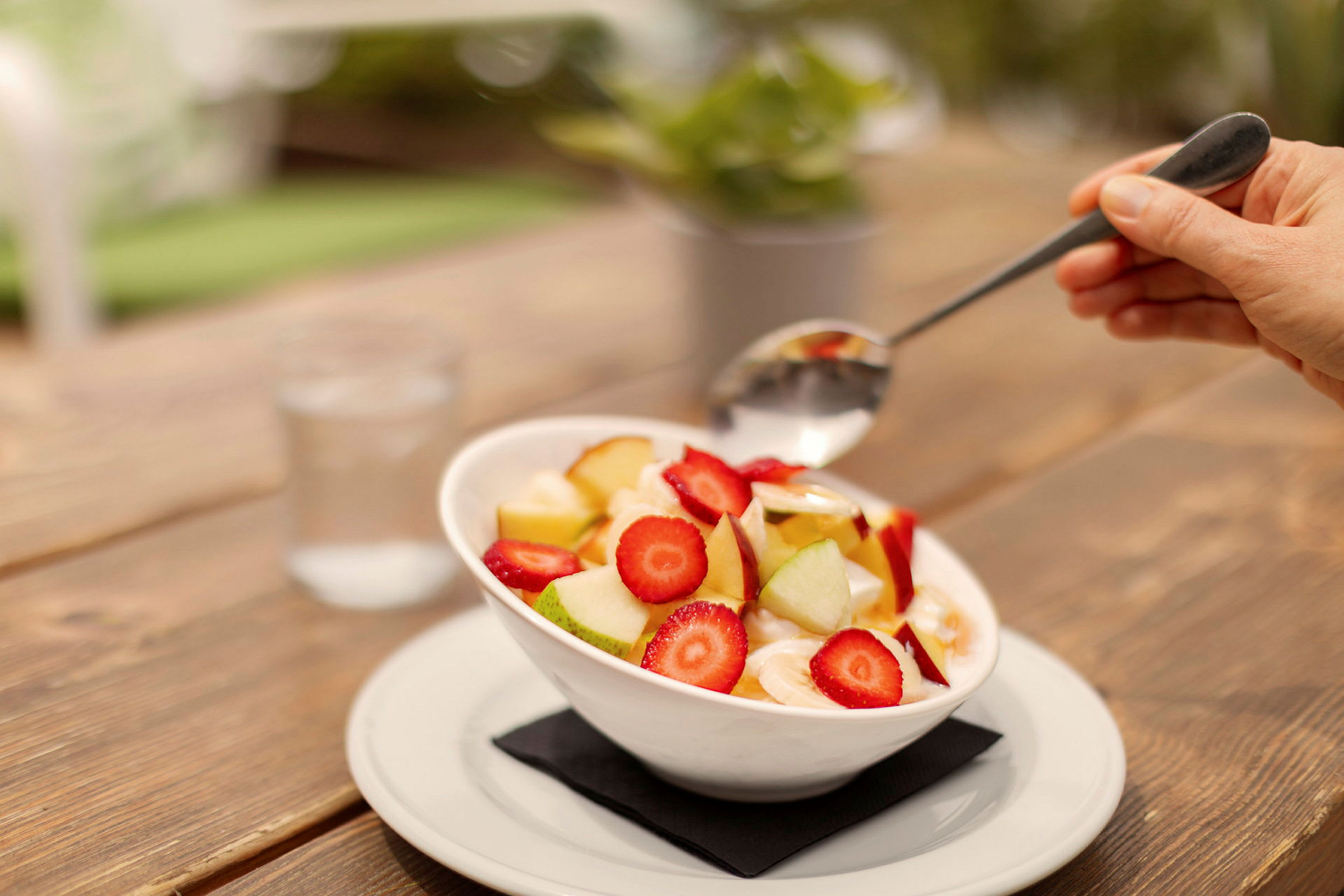 En skål med fruktsallad innehållande jordgubbar, äppelbitar och skivad banan, serverad på ett bord. (AI-genererad text)