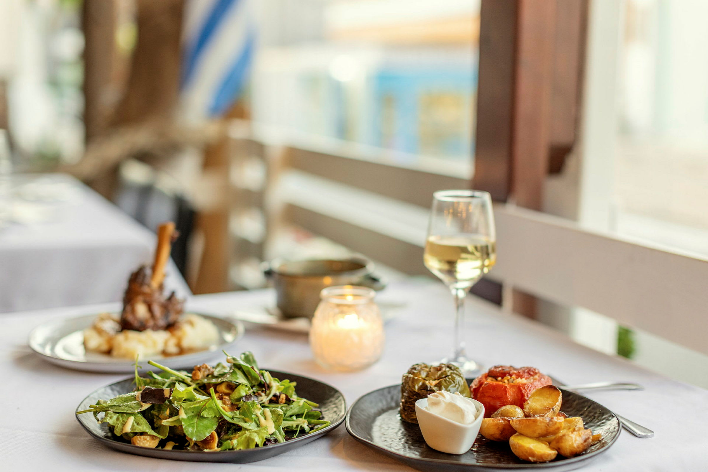 En bordsscen med mat uppdukad, inklusive sallad, fyllda grönsaker och potatis, samt ett glas vitt vin. (AI-genererad text)