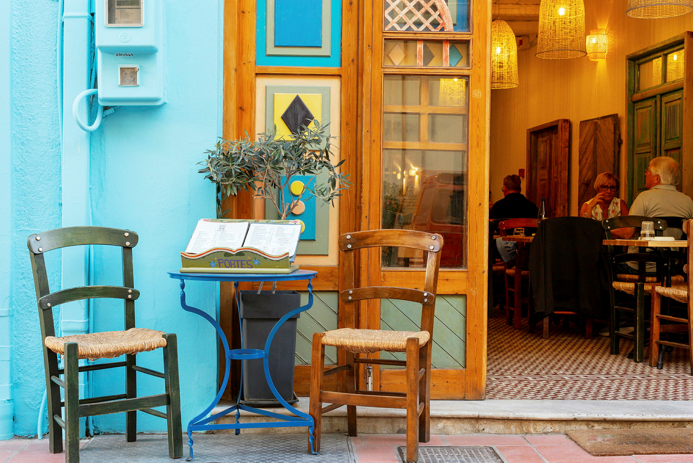 Entré till en restaurang med två trästolar och ett litet dekorativt bord utanför. (AI-genererad text)