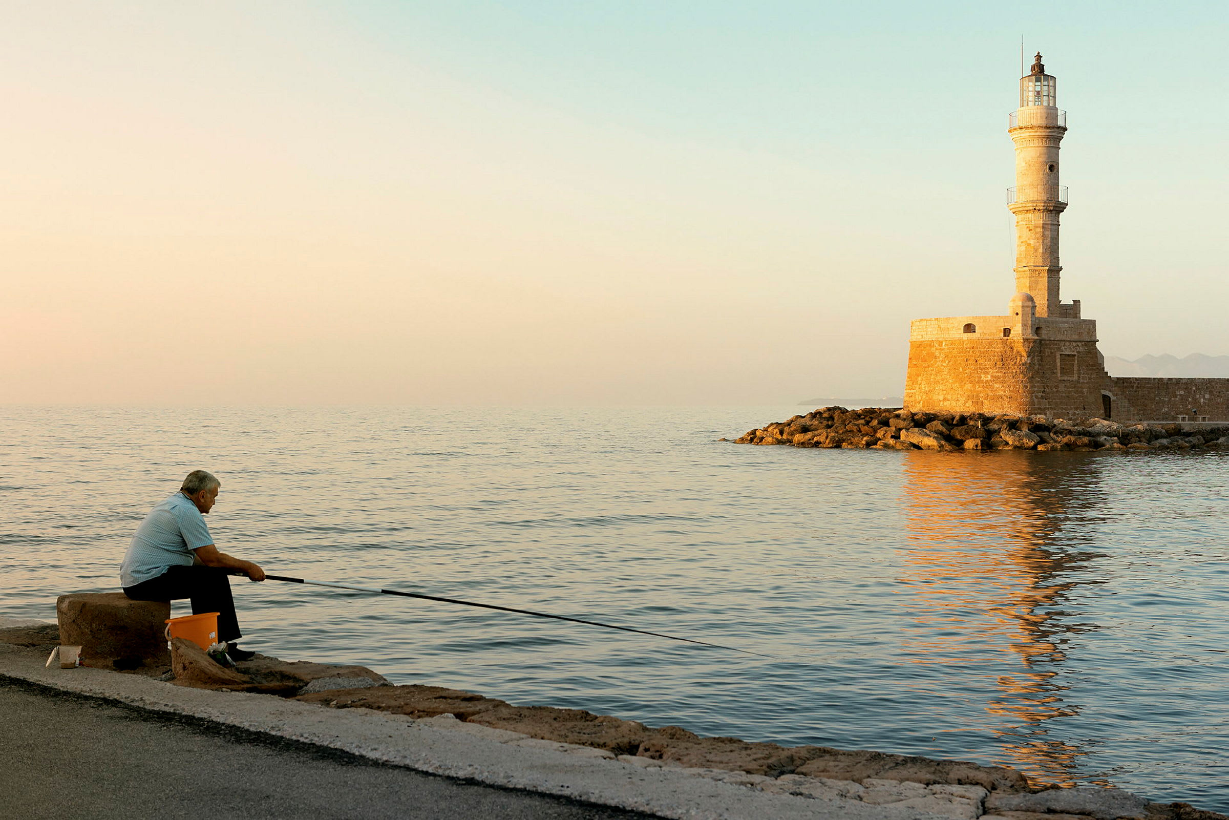 En person fiskar vid havet nära en stenpir med en fyr. (AI-genererad text)