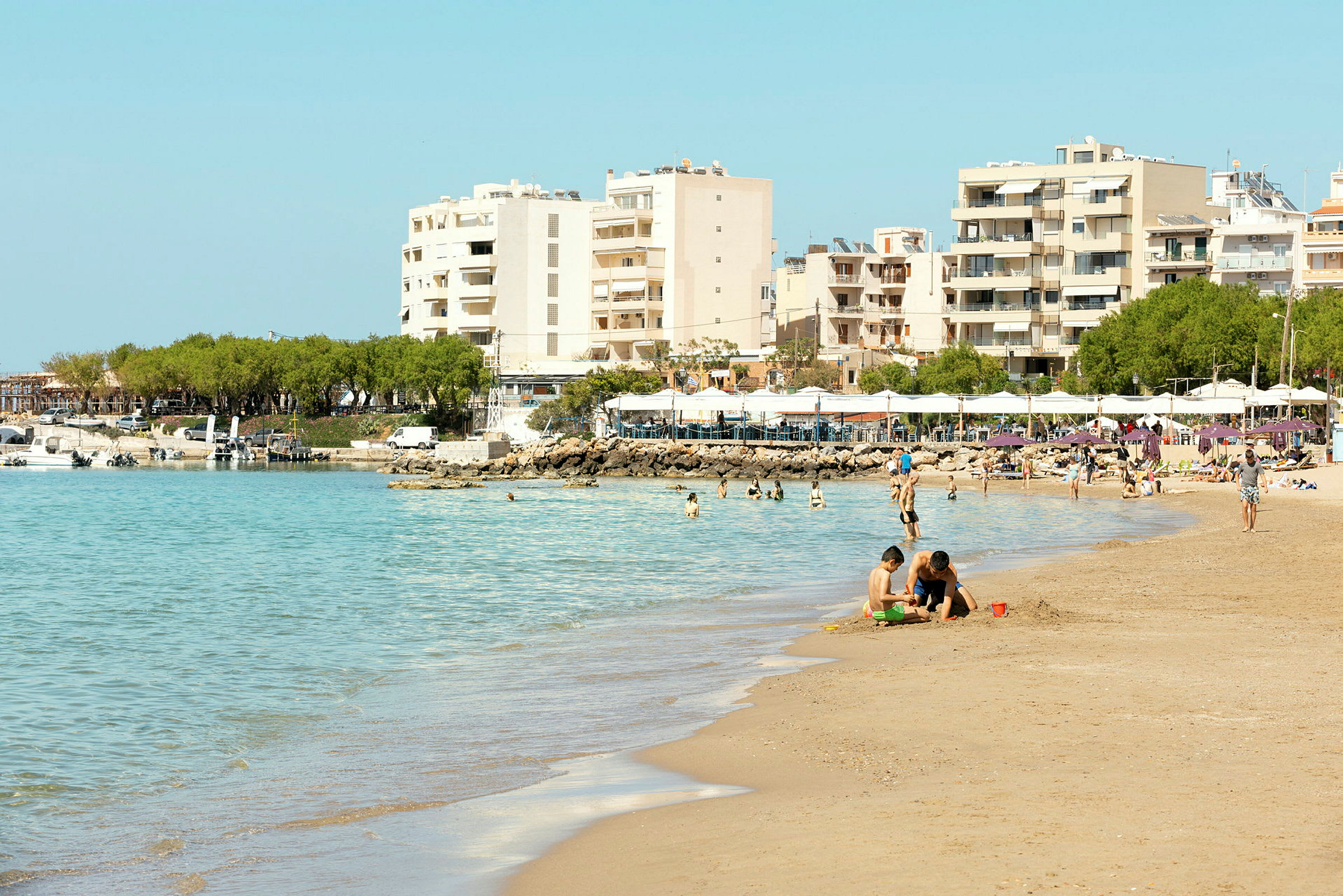 Bild på en strand med badande människor, byggnader i bakgrunden. (AI-genererad text)