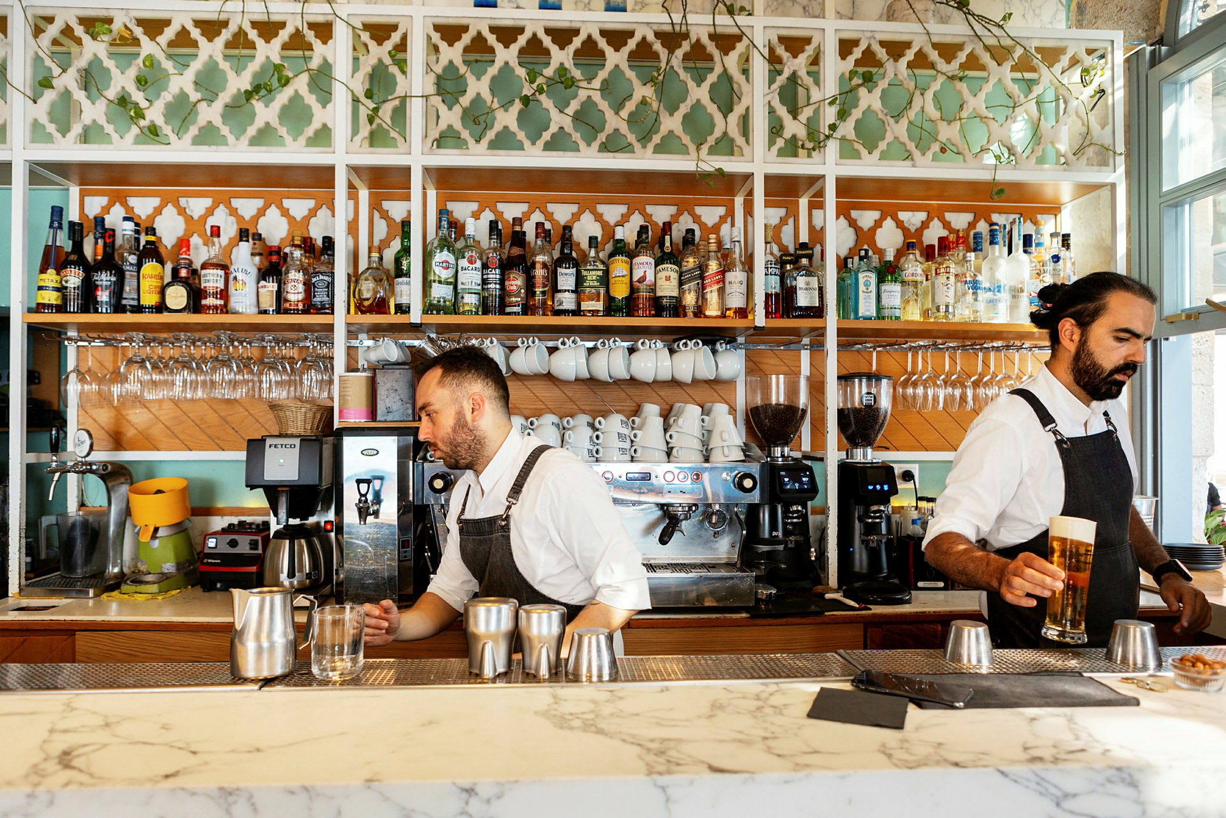 En bar med vitrinskåp fyllda med spritflaskor, kaffemuggar och glas. Kaffemaskiner står på bardisken. (AI-genererad text)