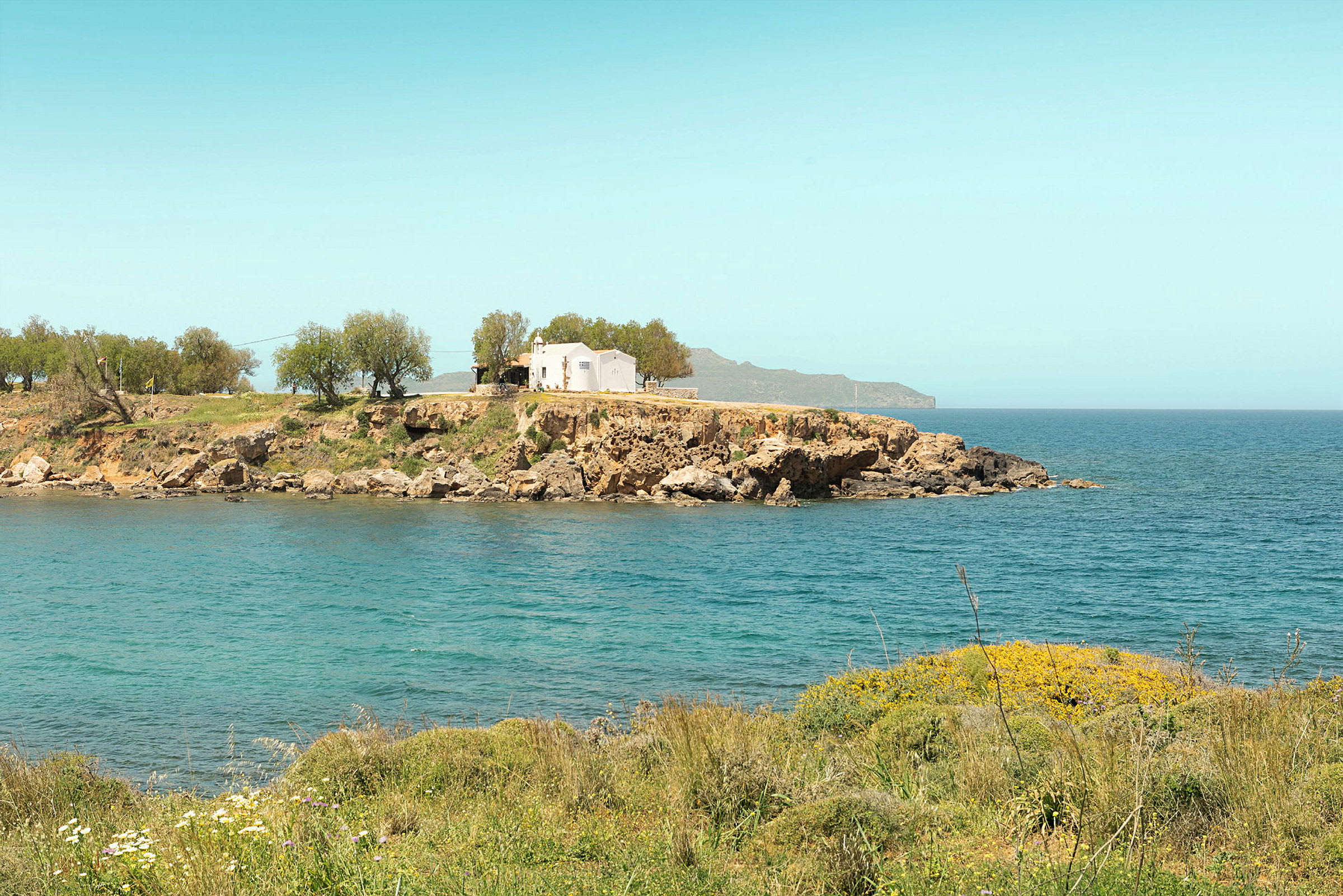 En vit byggnad på en klippa med hav och vegetation omkring. (AI-genererad text)
