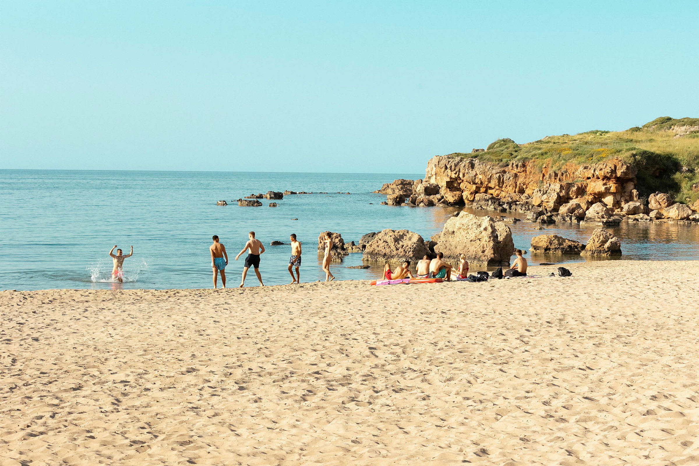 En sandstrand med människor som badar och slappnar av nära vattnet. (AI-genererad text)