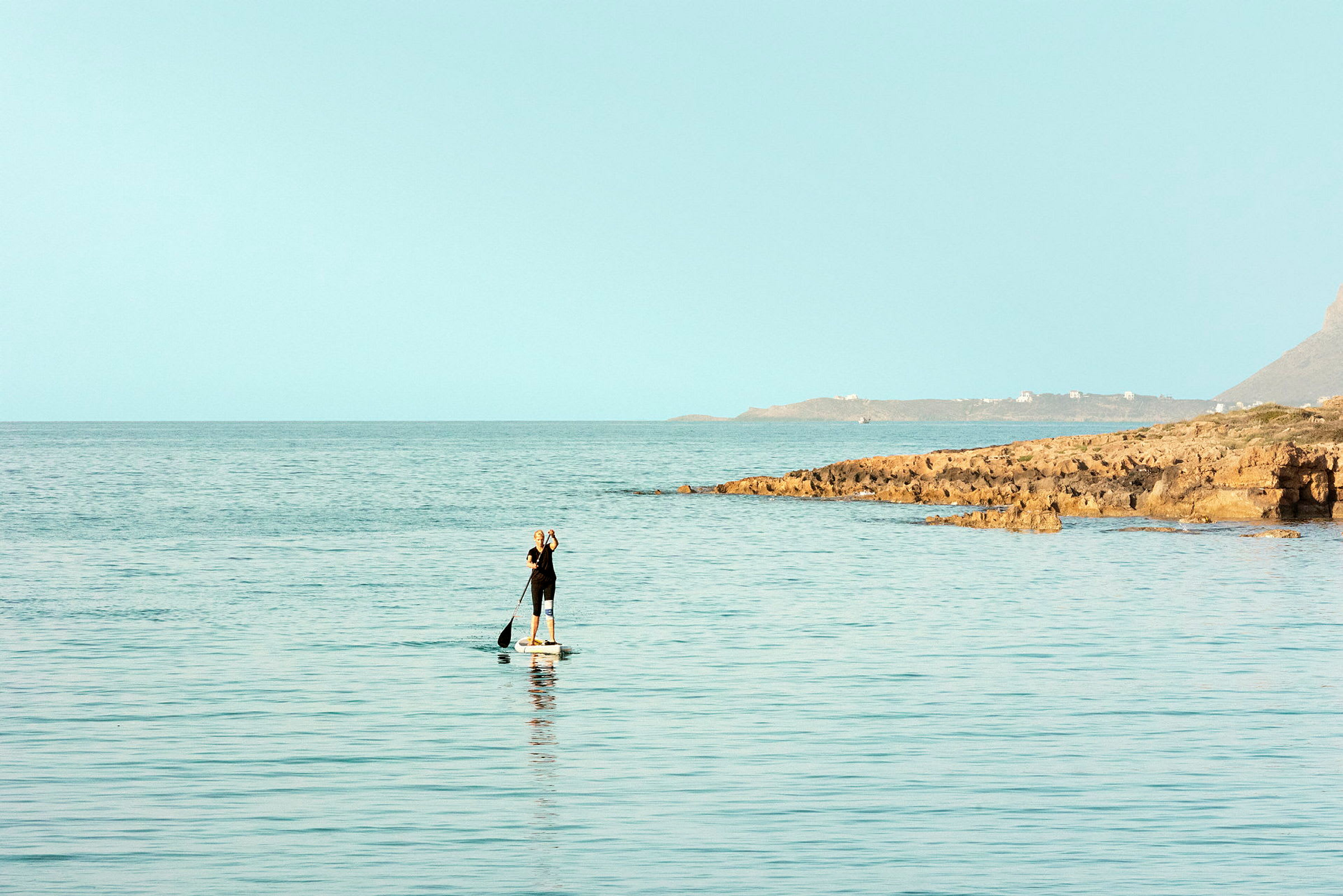 En person som paddlar på en paddleboard i havet nära en stenig kust. (AI-genererad text)