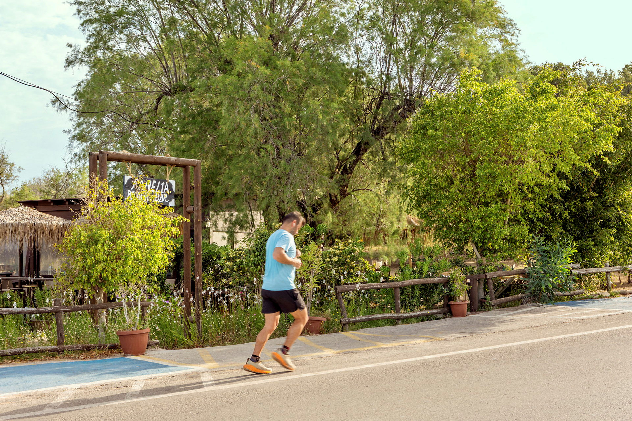 En person joggar på en väg nära gröna träd och en skylt för en restaurang. (AI-genererad text)