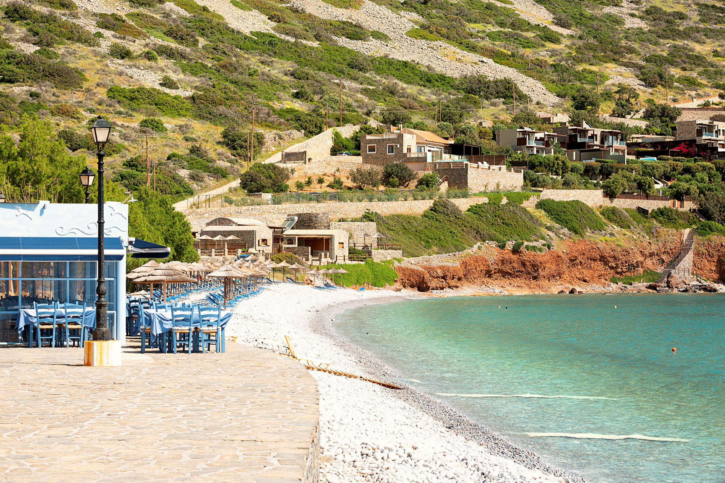 Strand med stenar, havet och hus i bakgrunden. (AI-genererad text)