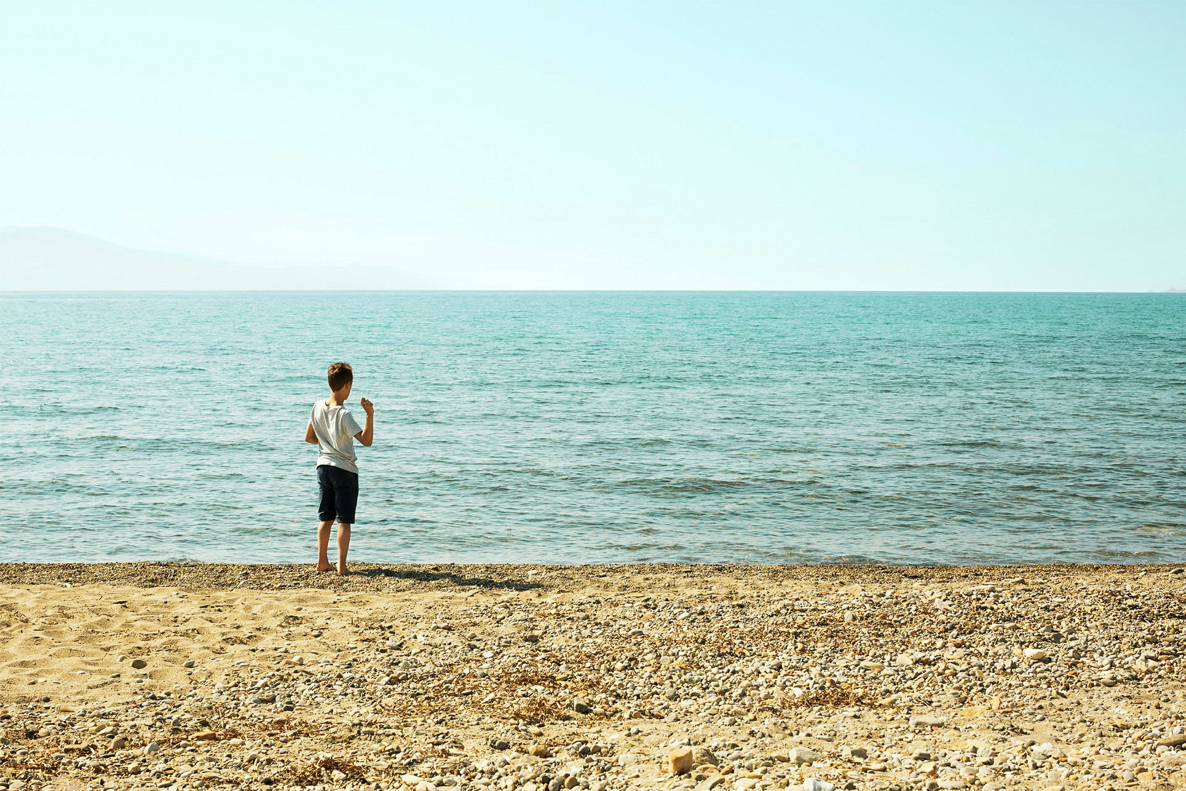Ett barn står på en stenig strand och tittar ut över havet. (AI-genererad text)