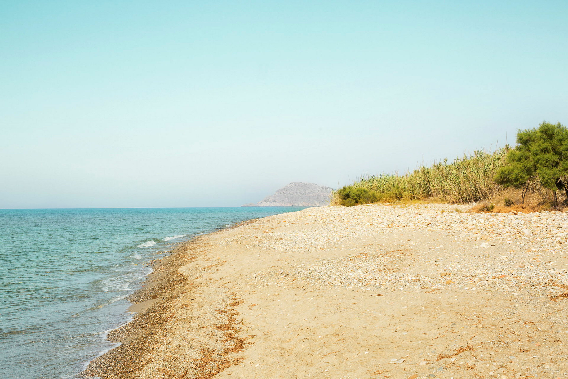 En sandstrand med klippor vid sidan av havet, omgärdad av grön vegetation. (AI-genererad text)