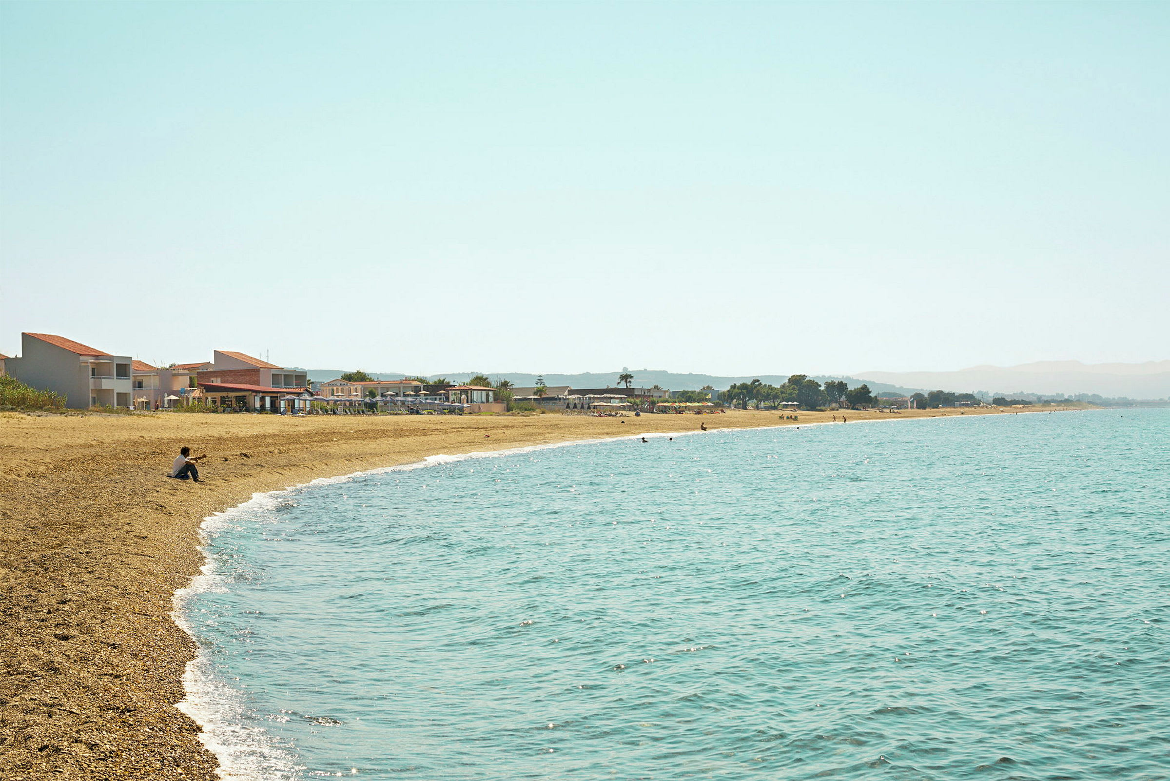 Strand med klart vatten och byggnader i bakgrunden. (AI-genererad text)