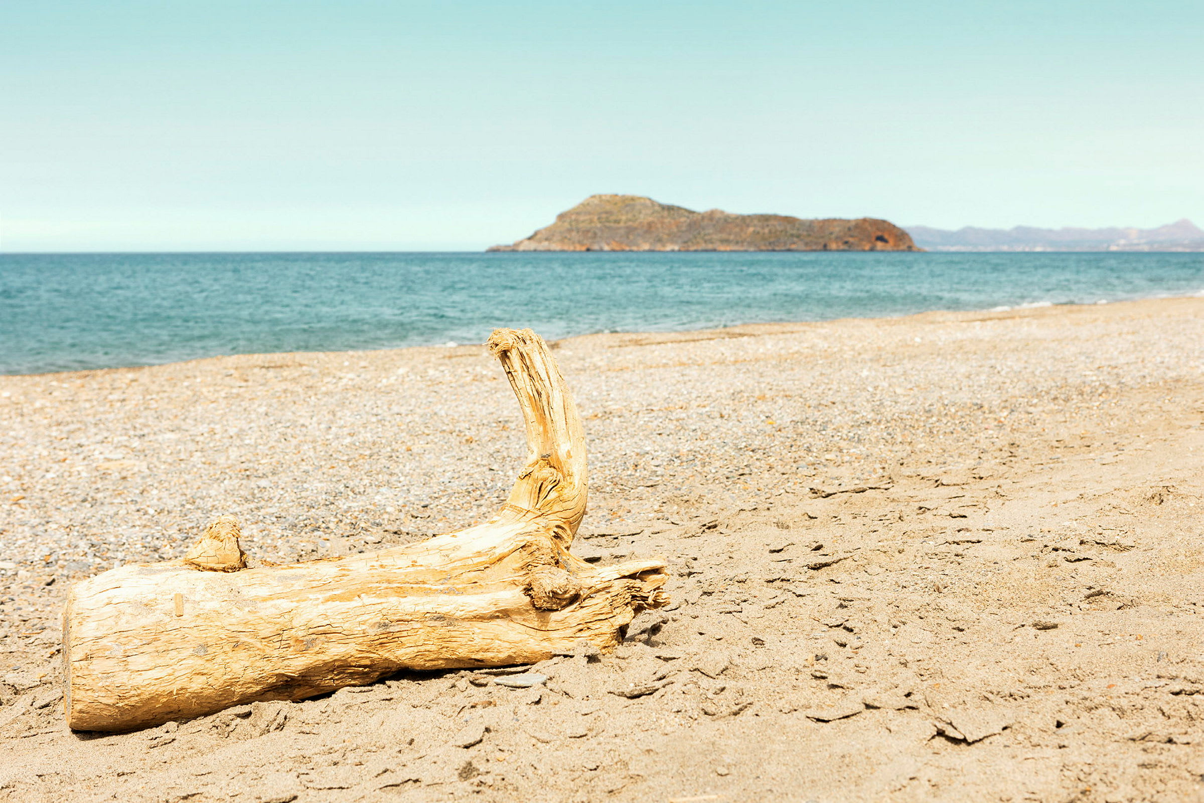En träbit ligger på stranden med havet och en bergig ö i bakgrunden. (AI-genererad text)
