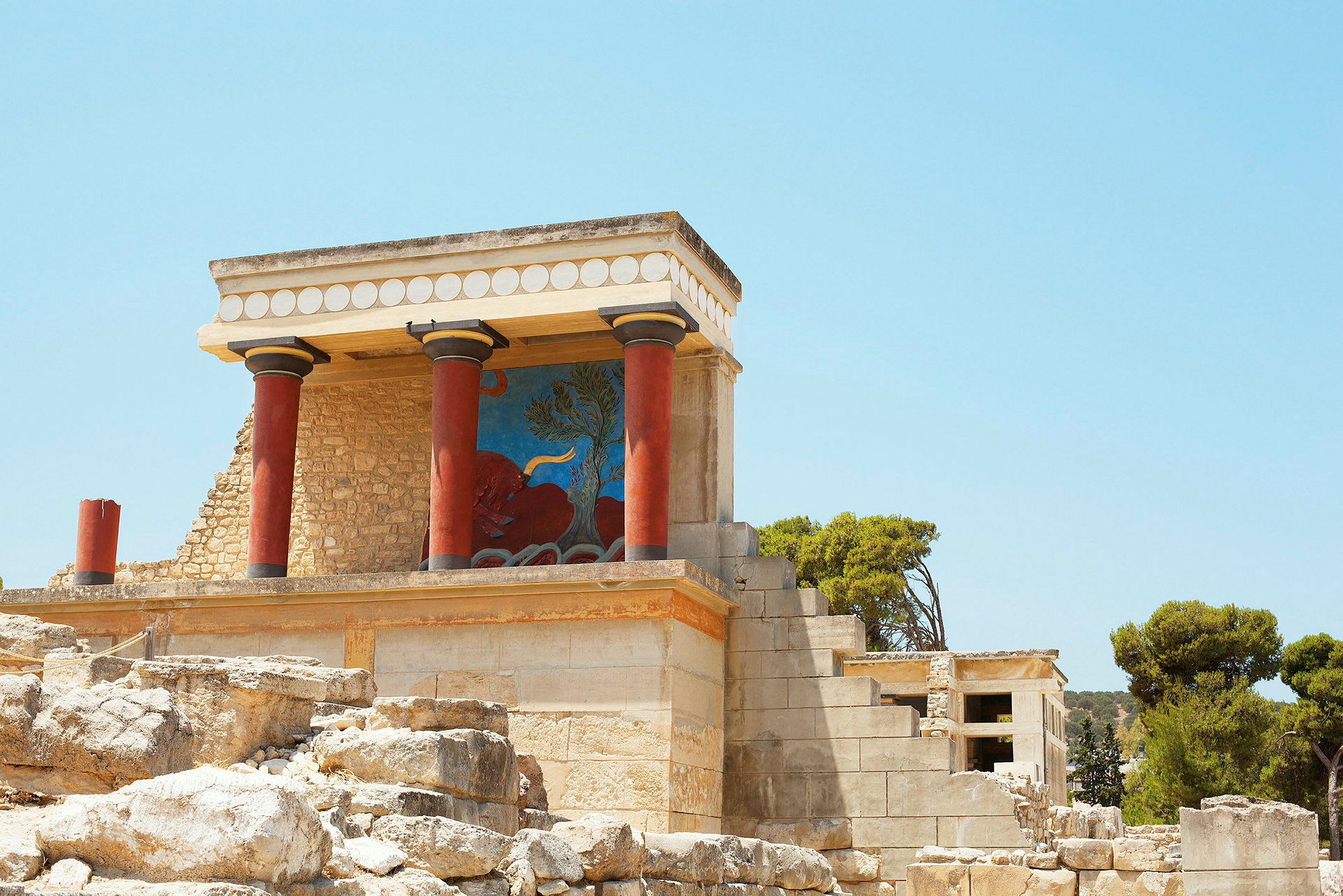 Knossos palats med röda pelare och färgstarka utsmyckningar under en klar blå himmel. (AI-genererad text)