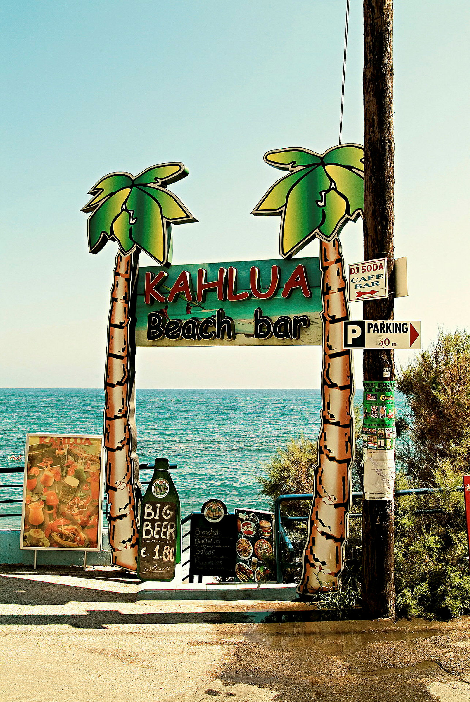 Bild på skylt med texten 'Kahlua Beach Bar' framför havet. (AI-genererad text)