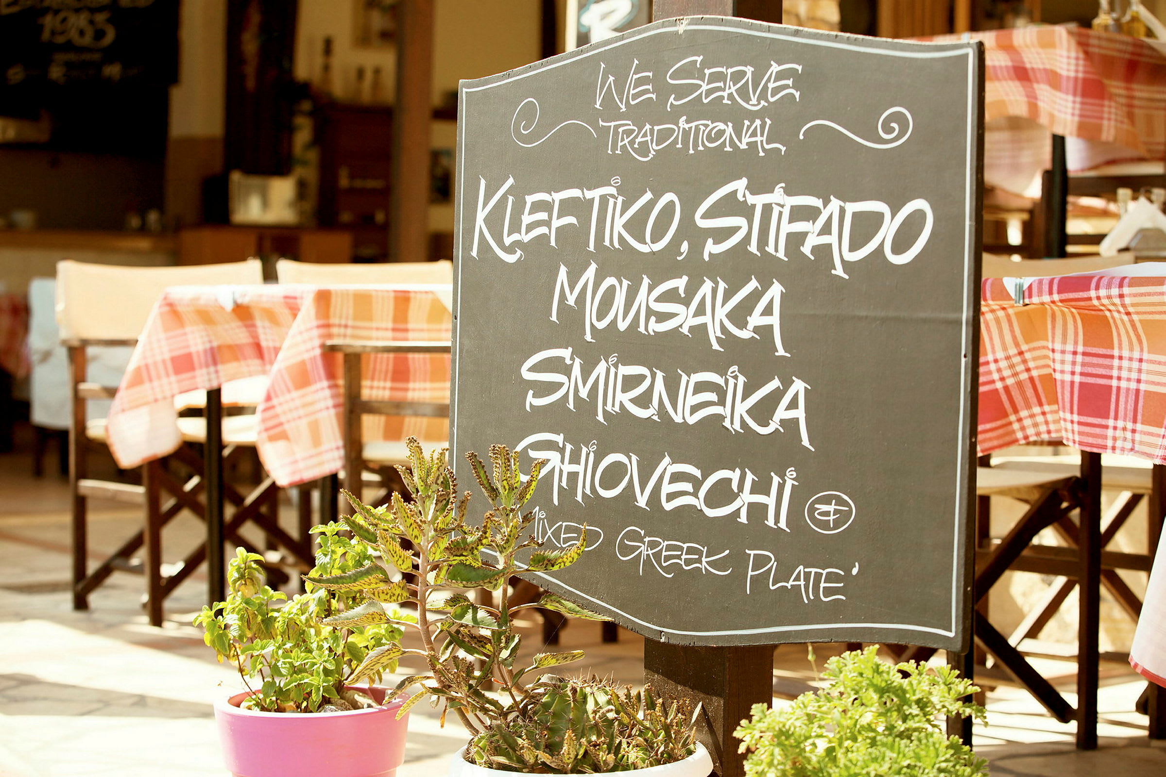 Ett skylt utanför en restaurang med texten som listar traditionella grekiska maträtter. (AI-genererad text)