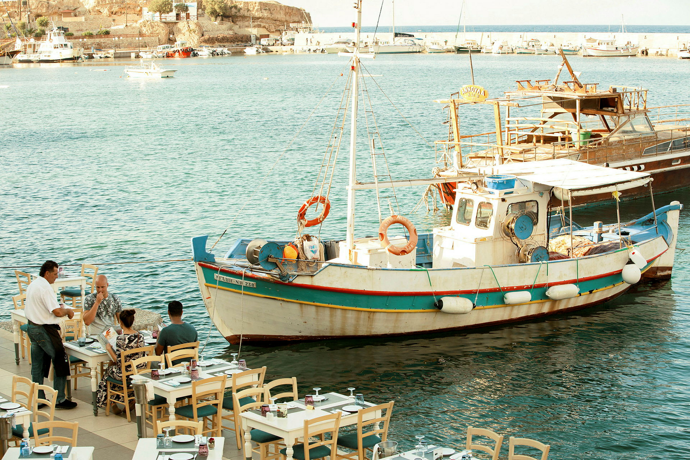 En fiskebåt ligger förtöjd vid en brygga nära en restaurang vid havet. (AI-genererad text)