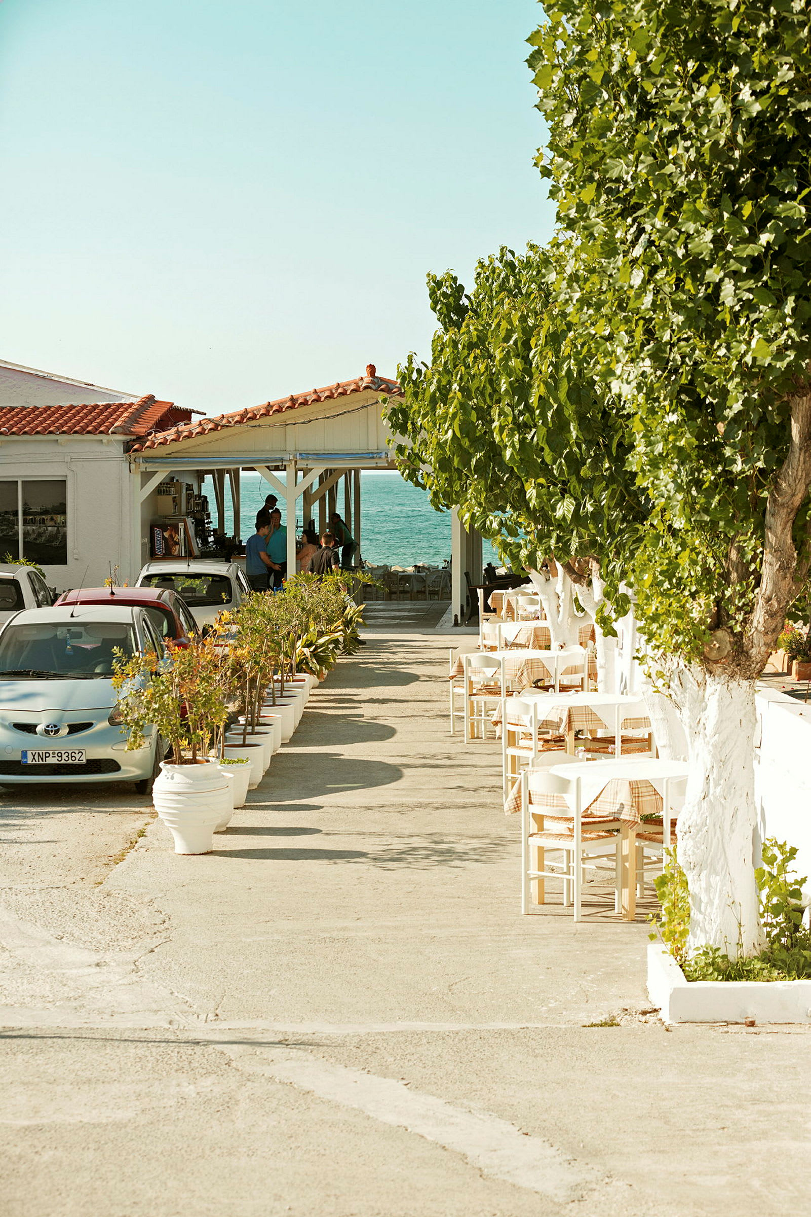 Ett café vid havet med uteservering och parkerade bilar. (AI-genererad text)