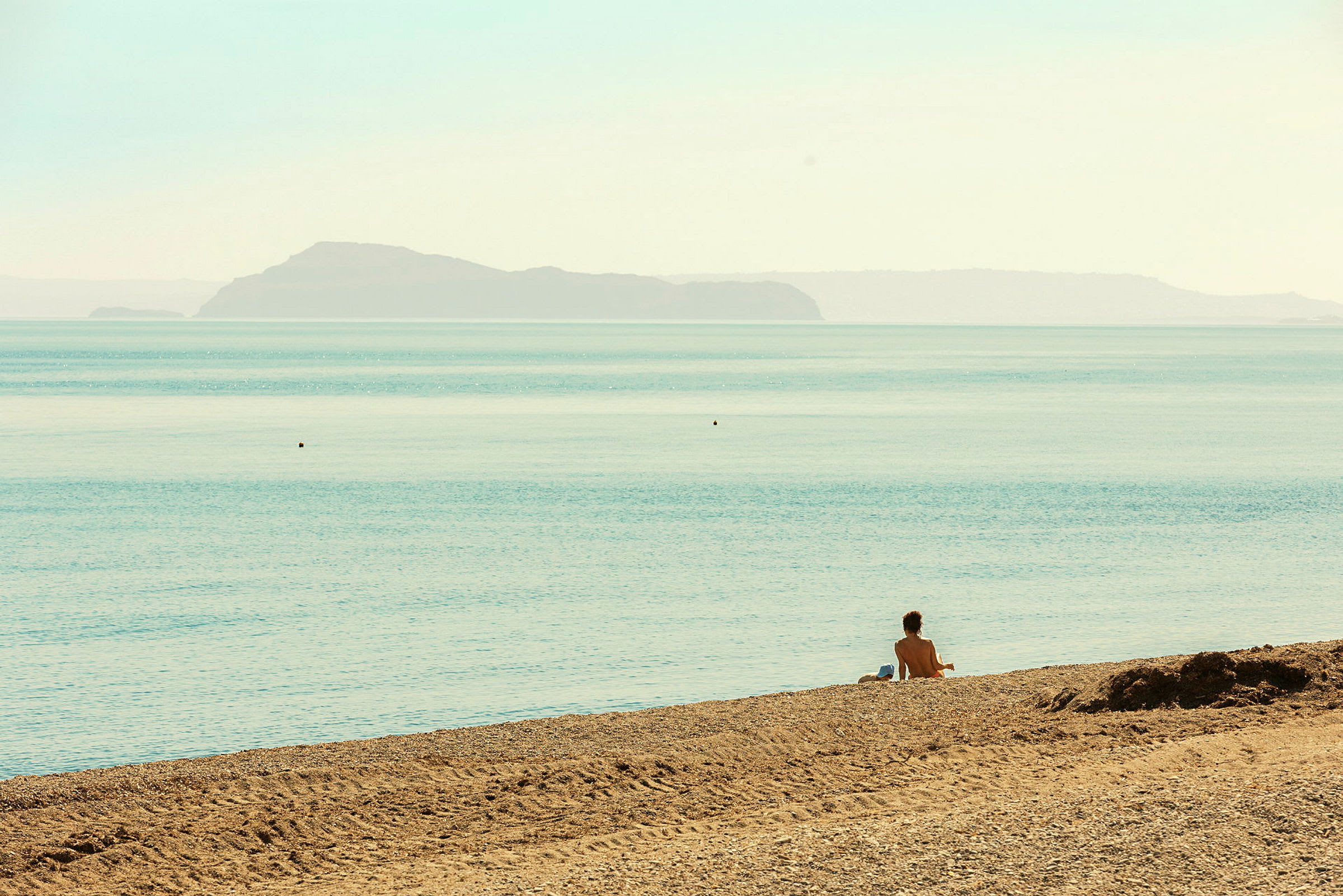 En person sitter på en sandstrand vid havet med en ö i bakgrunden. (AI-genererad text)