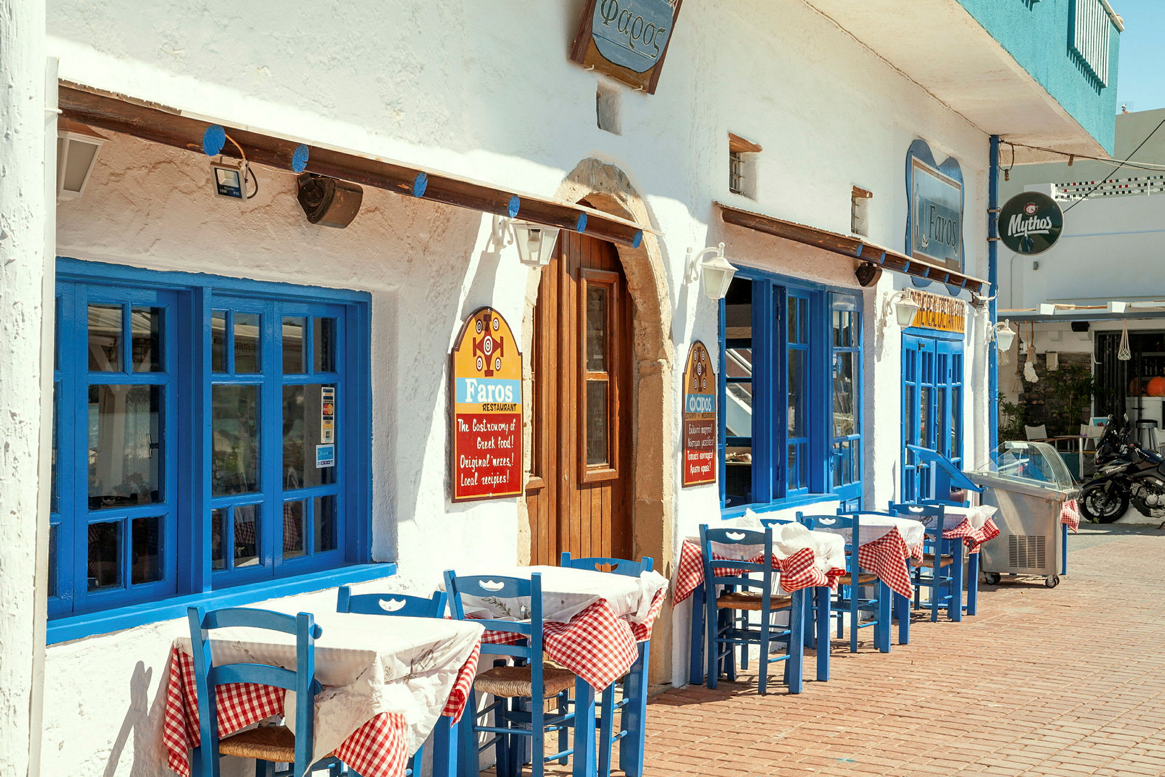 En restaurang med blå dörrar, fönster och utemöbler, belägen vid en gata. (AI-genererad text)