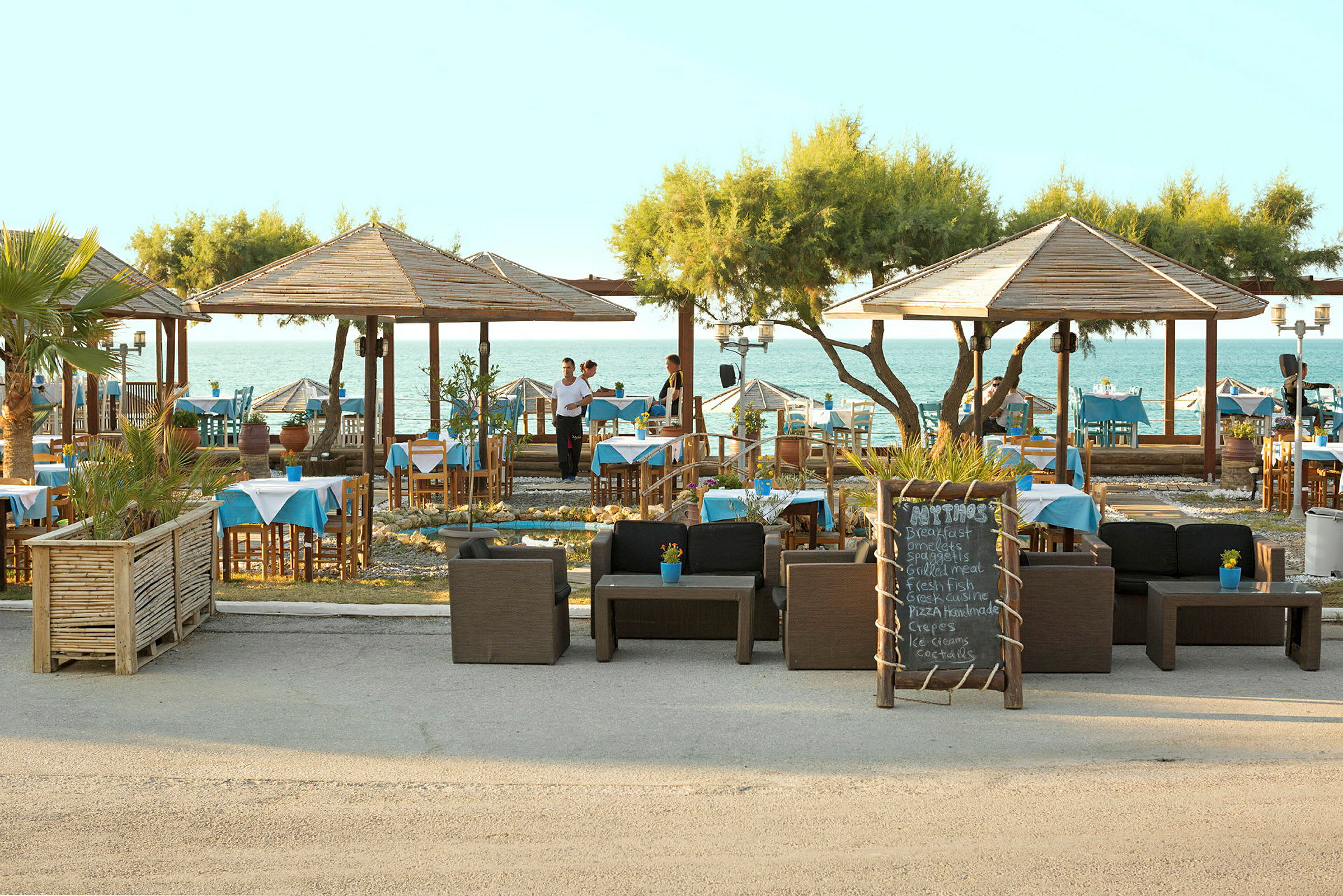 Restaurang vid stranden med bord, stolar och skylt. (AI-genererad text)