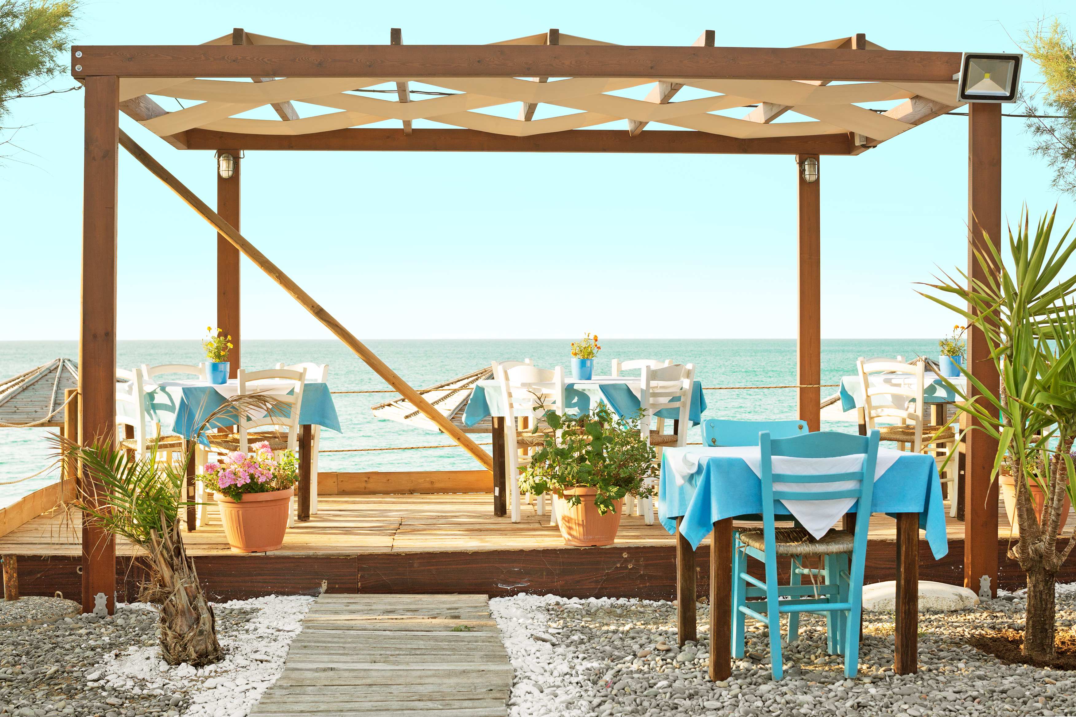 En restaurang nära havet med träpergola och blå dukar på borden. (AI-genererad text)