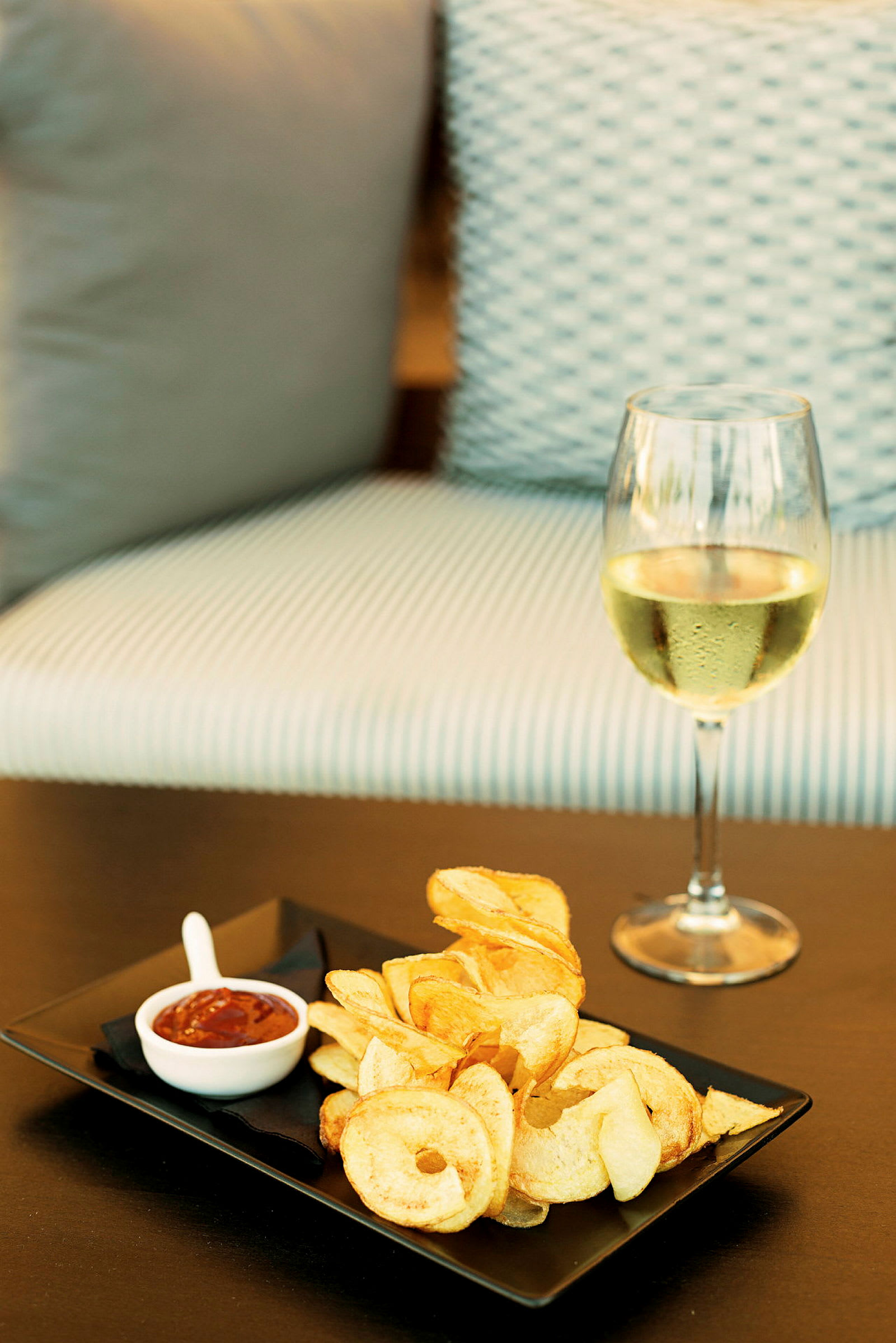 Ett glas vitt vin bredvid en tallrik med chips och dip. (AI-genererad text)