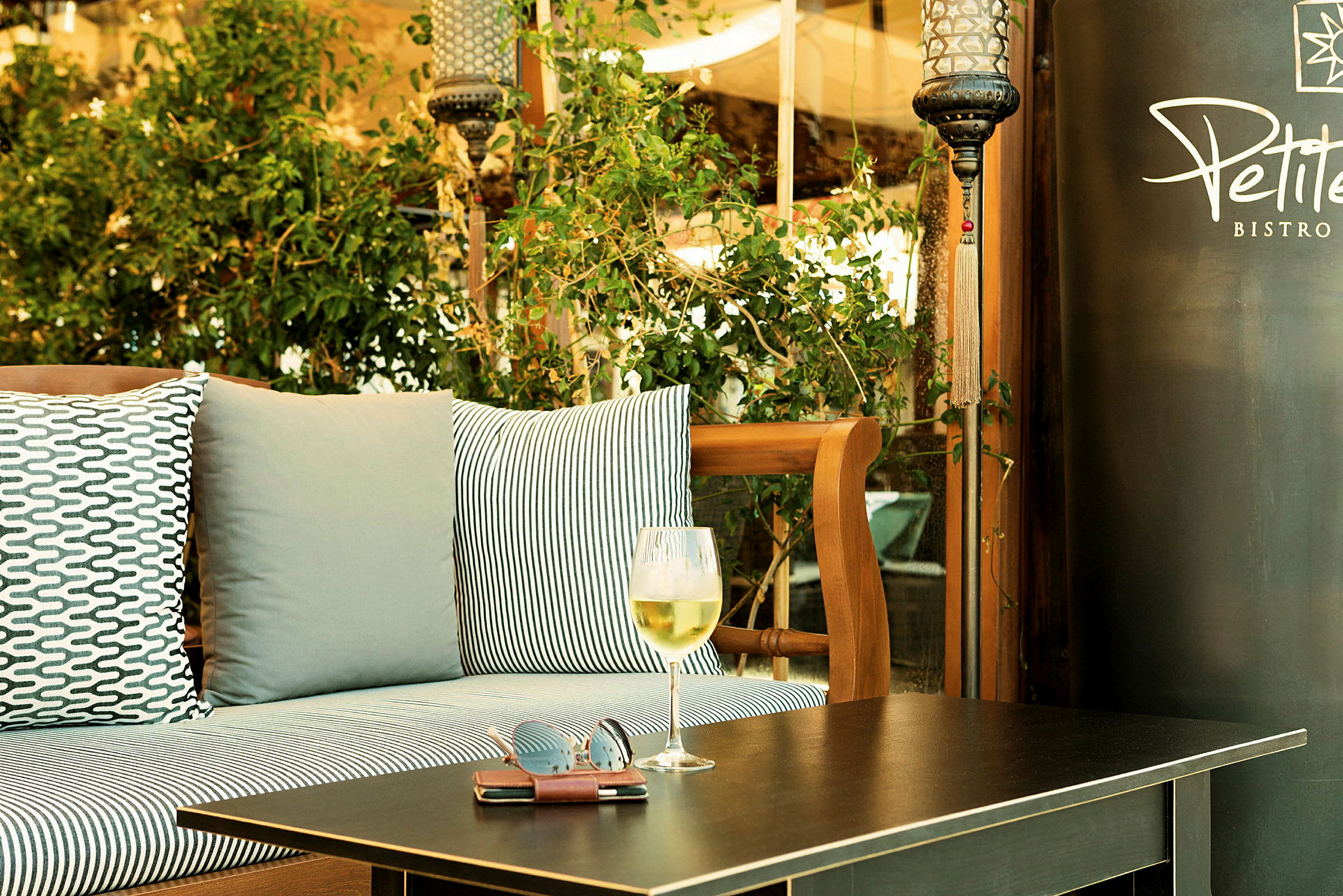 Utomhusmiljö med sittplats, kuddar och ett bord med ett glas vin och solglasögon. (AI-genererad text)
