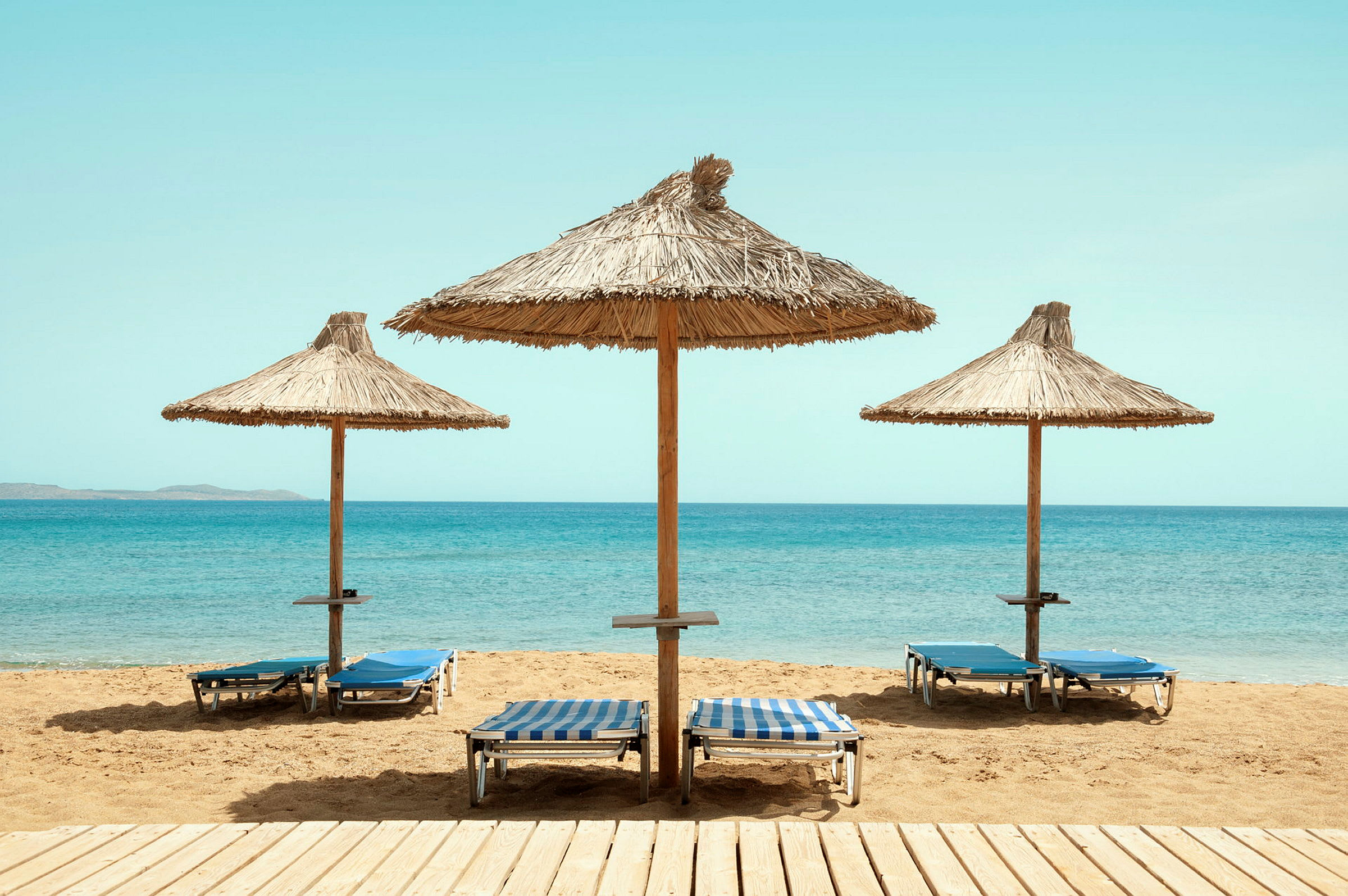 Tre solparasoller med solstolar på en sandstrand vid havet. (AI-genererad text)