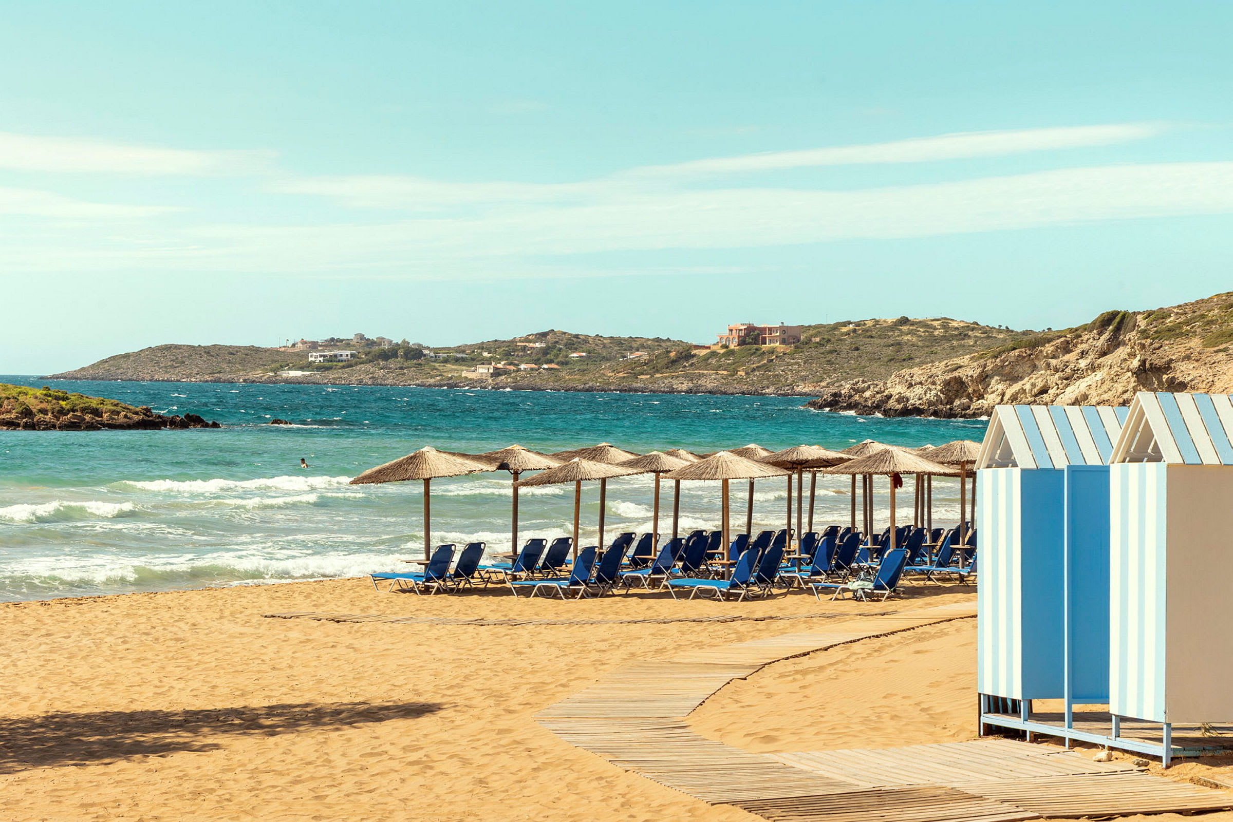 Strand med parasoller och solstolar, en strandpromenad i trä och små färgglada strandbodar. (AI-genererad text)