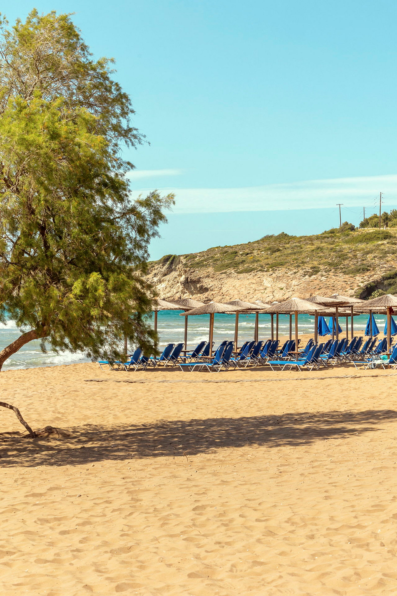 Strand med sand, solparasoller och solstolar samt en trädkant i förgrunden. (AI-genererad text)
