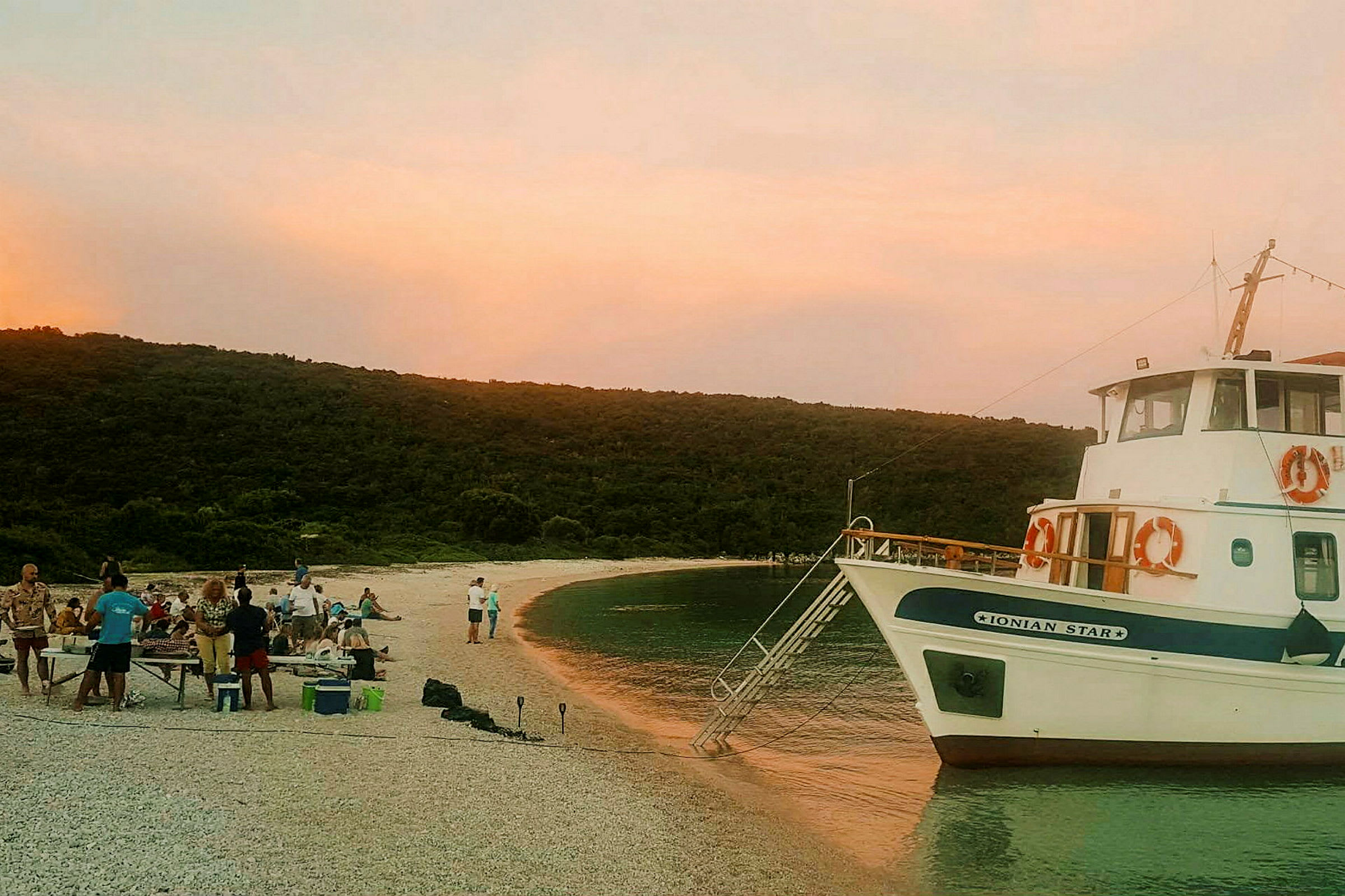 En båt ligger förtöjd vid en strand medan folk samlas på stranden i solnedgångens sken. (AI-genererad text)