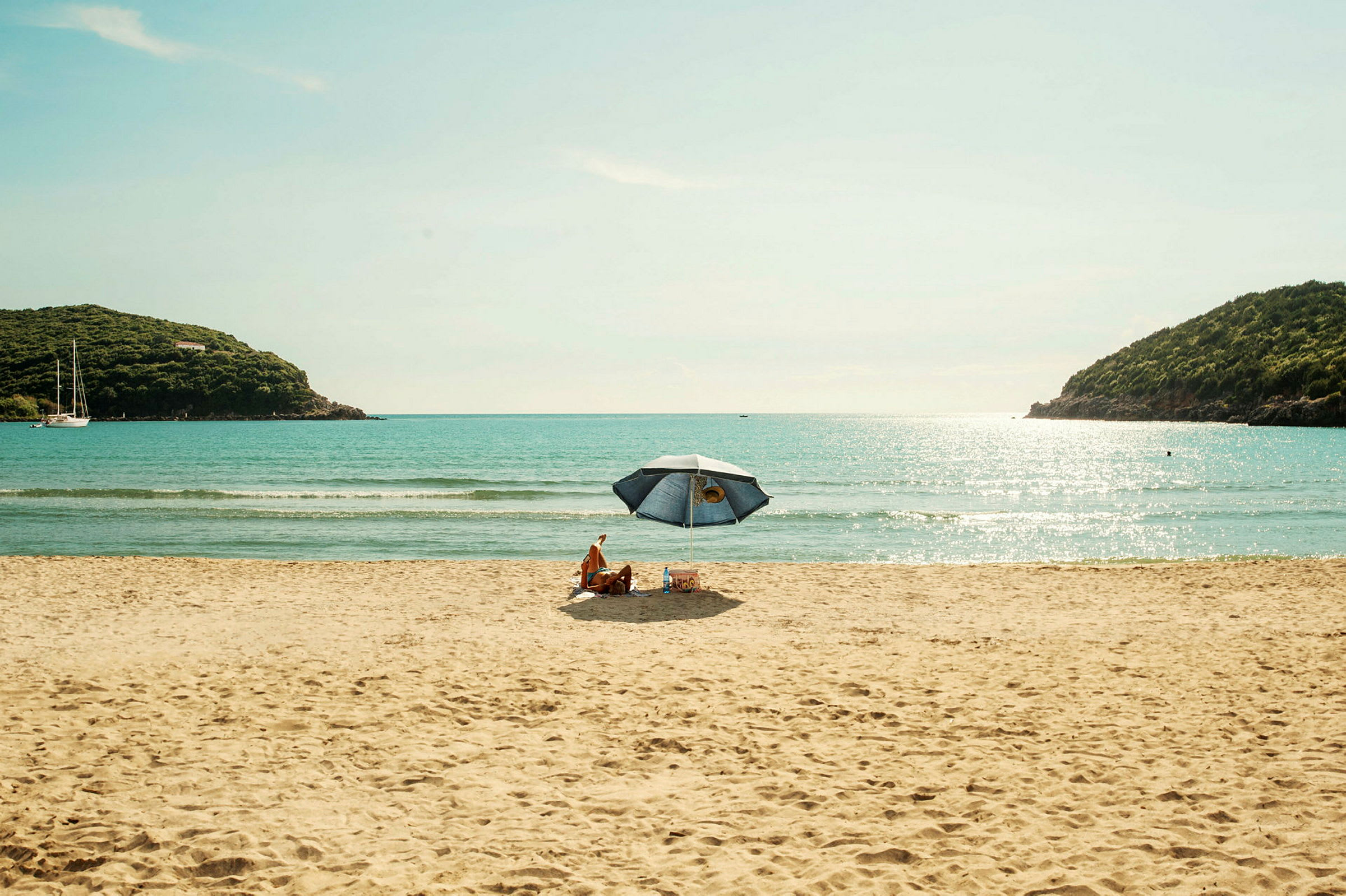 Personer sitter under ett parasoll på en sandstrand med havet i bakgrunden. (AI-genererad text)
