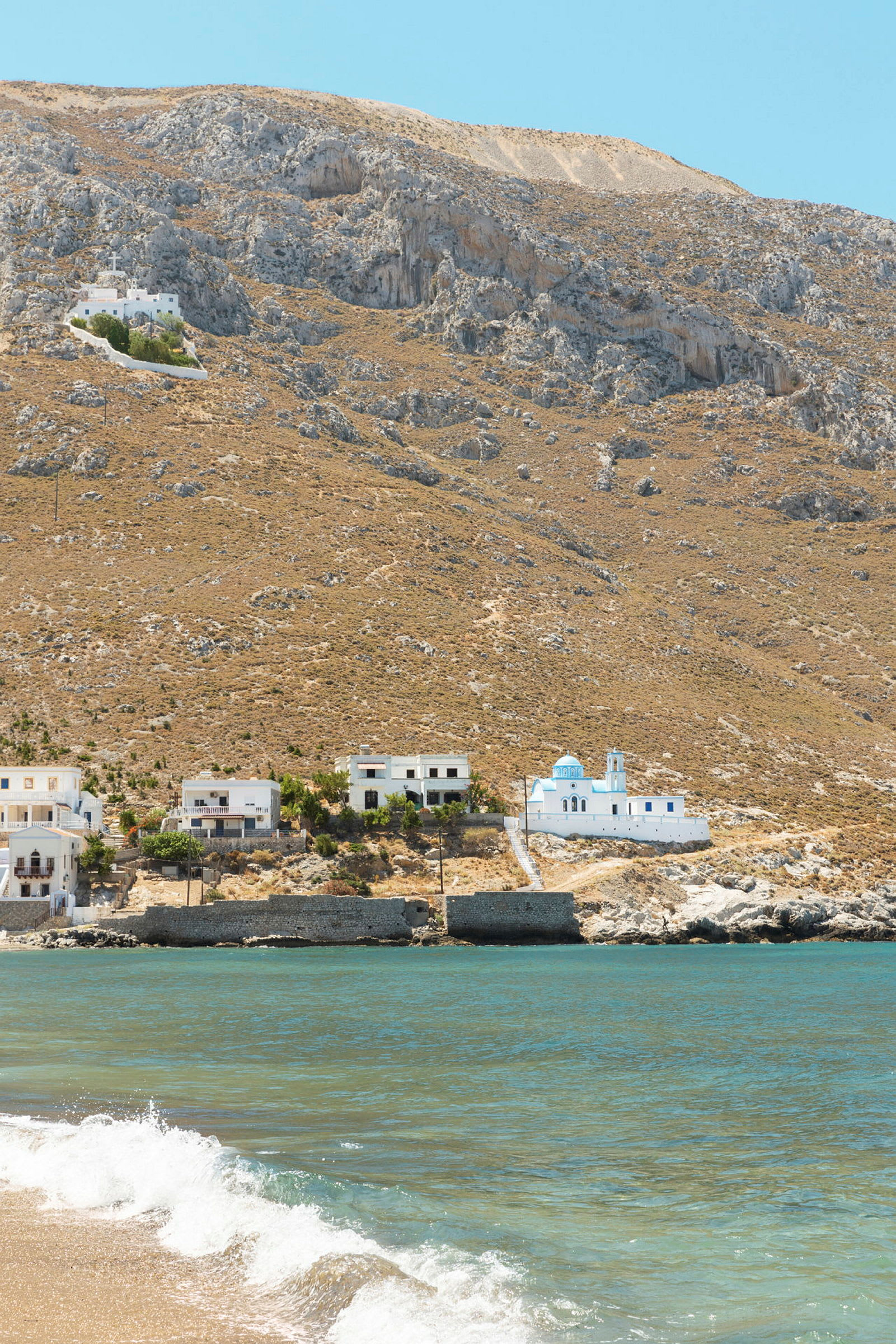 Strand med hav, byggnader och bergskulle i bakgrunden. (AI-genererad text)