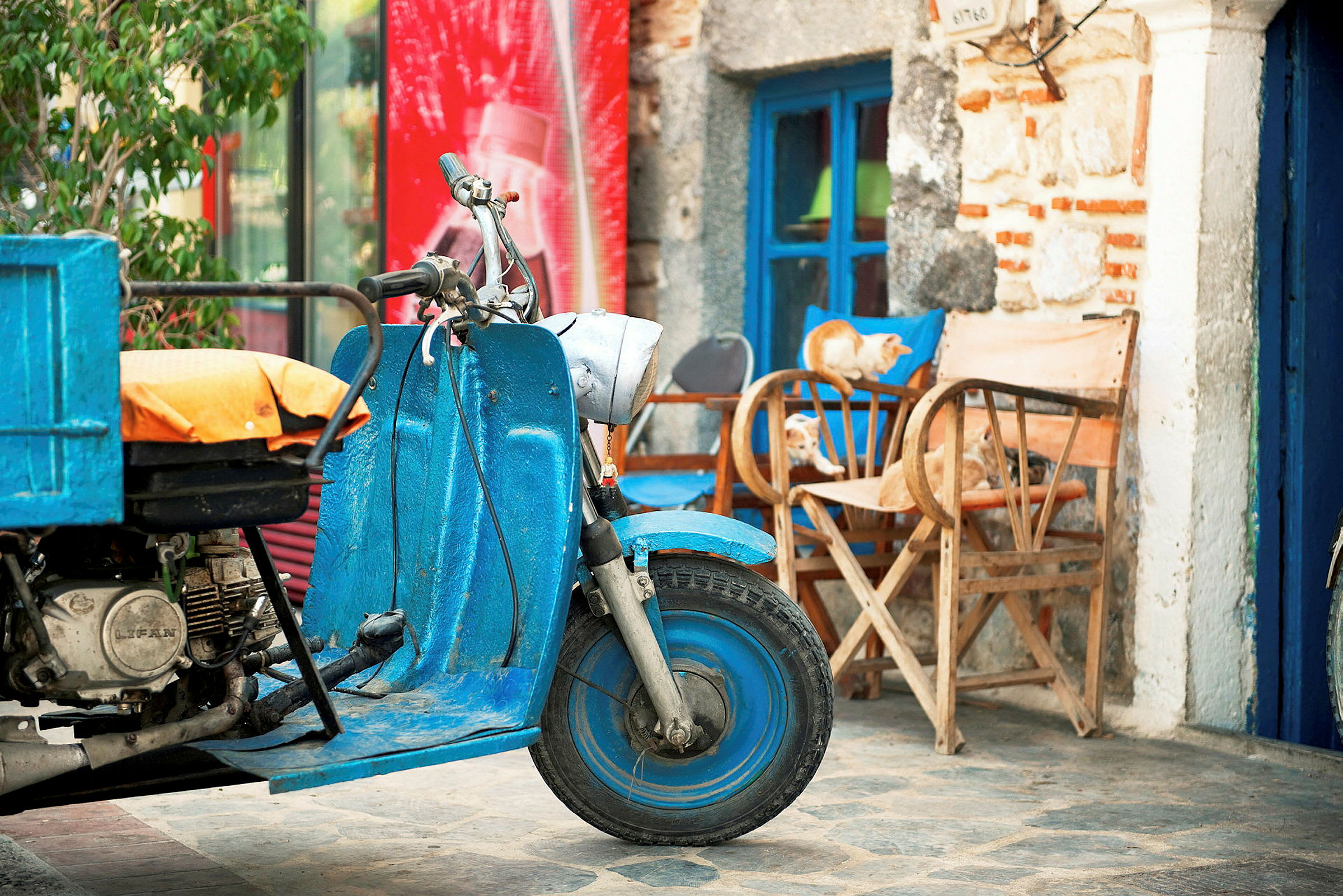 Blå motorcykel med lastflak står framför möbler och en byggnad. (AI-genererad text)