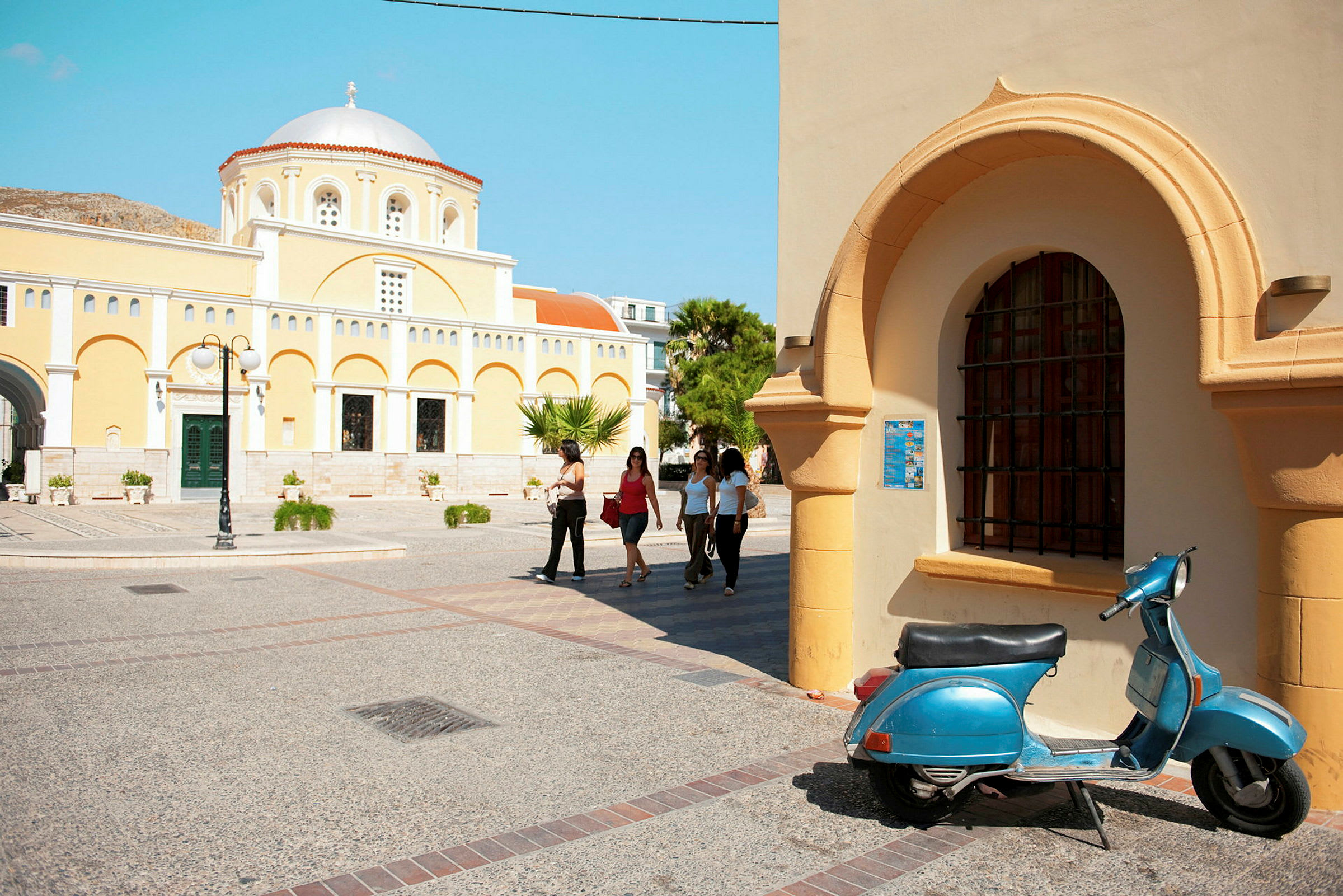Gult kyrkligt byggnad med välvt tak, arkitektoniska detaljer och ett blått scooter i förgrunden. (AI-genererad text)