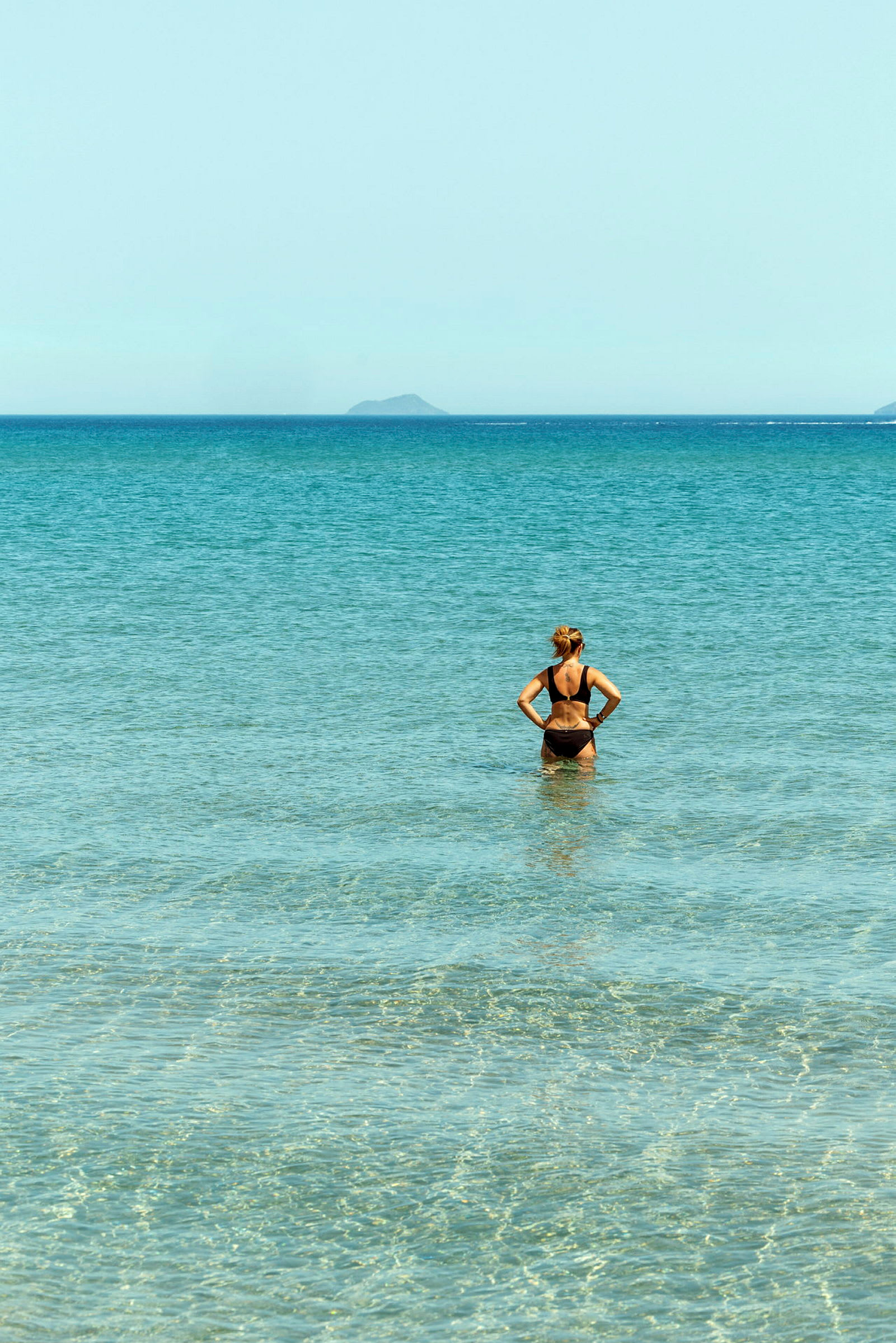 En person står i klart vatten och blickar mot havet. (AI-genererad text)