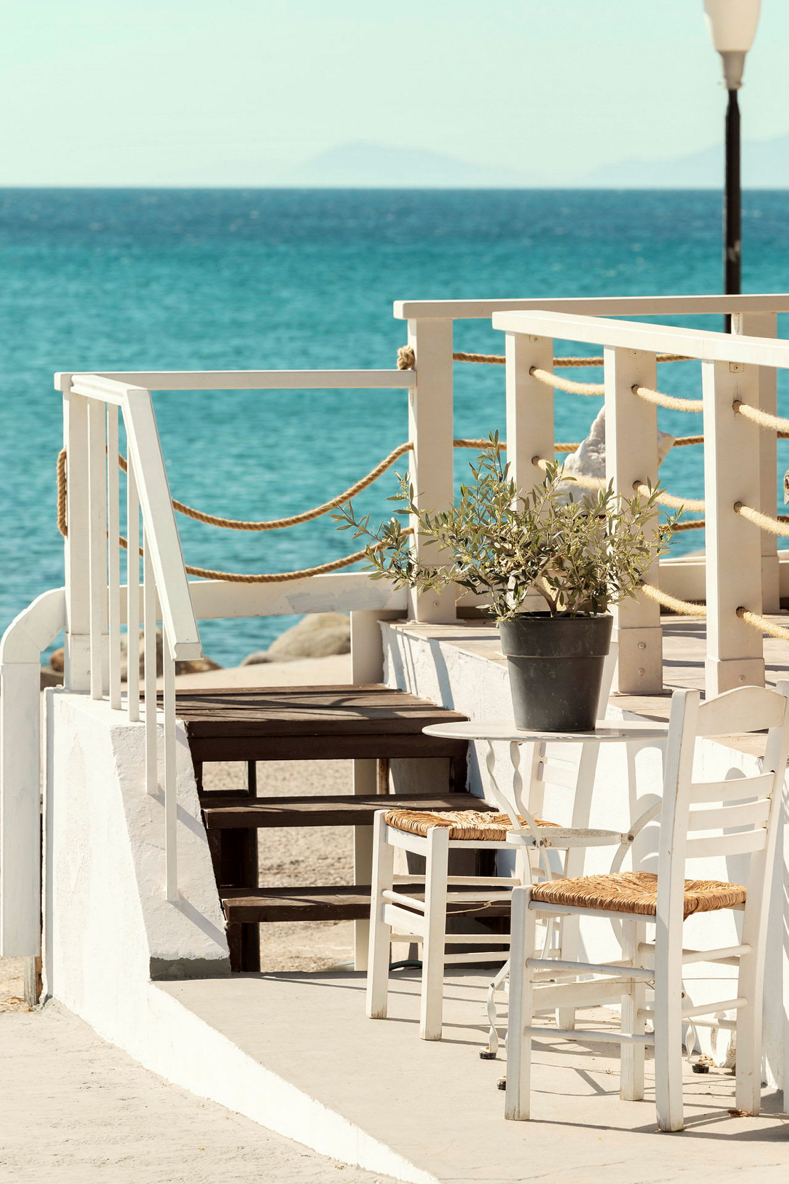 En vit veranda med ett bord och stolar nära vattnet. (AI-genererad text)