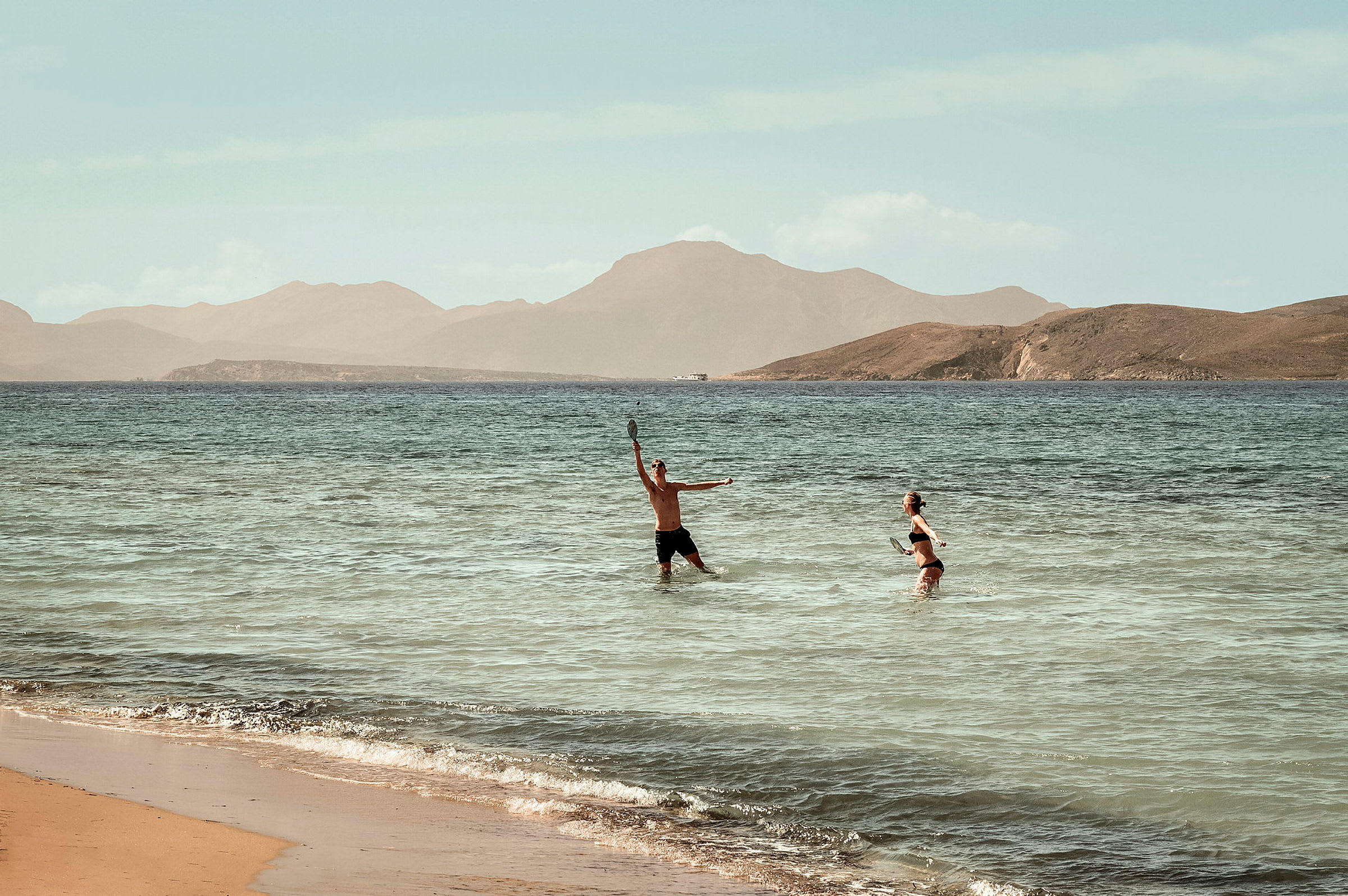 Två personer spelar strandtennis i vattnet vid en strand. (AI-genererad text)