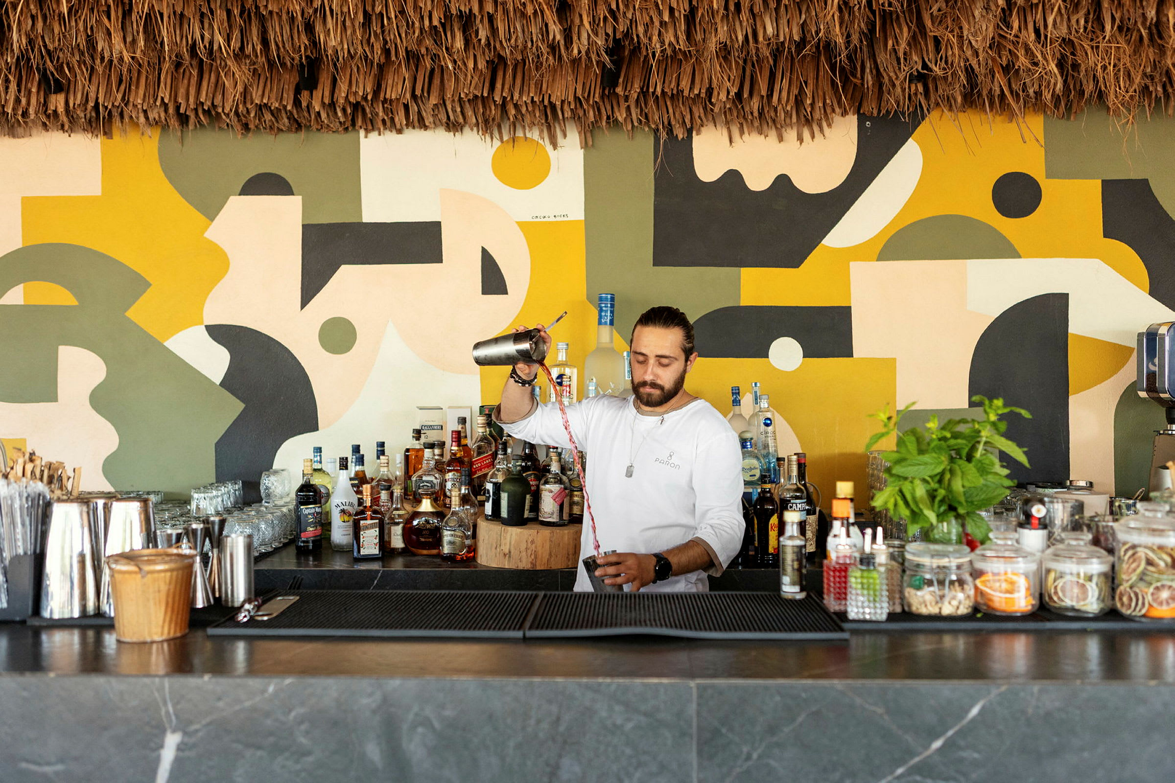 En bartender förbereder en drink bakom en bar med färgglad väggdekor. (AI-genererad text)