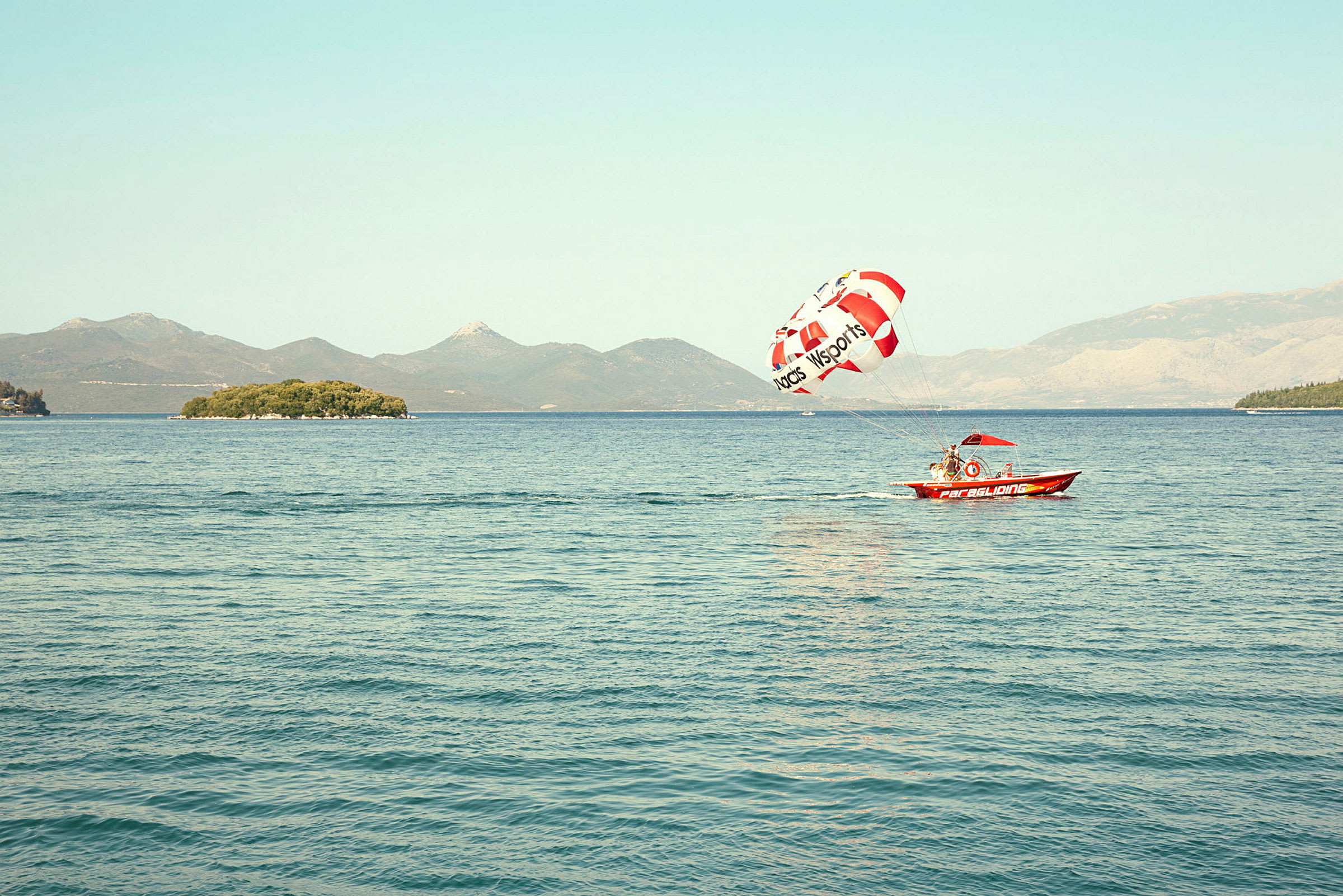 En liten motorbåt drar en parasailing skärm över vatten med en ö i bakgrunden. (AI-genererad text)
