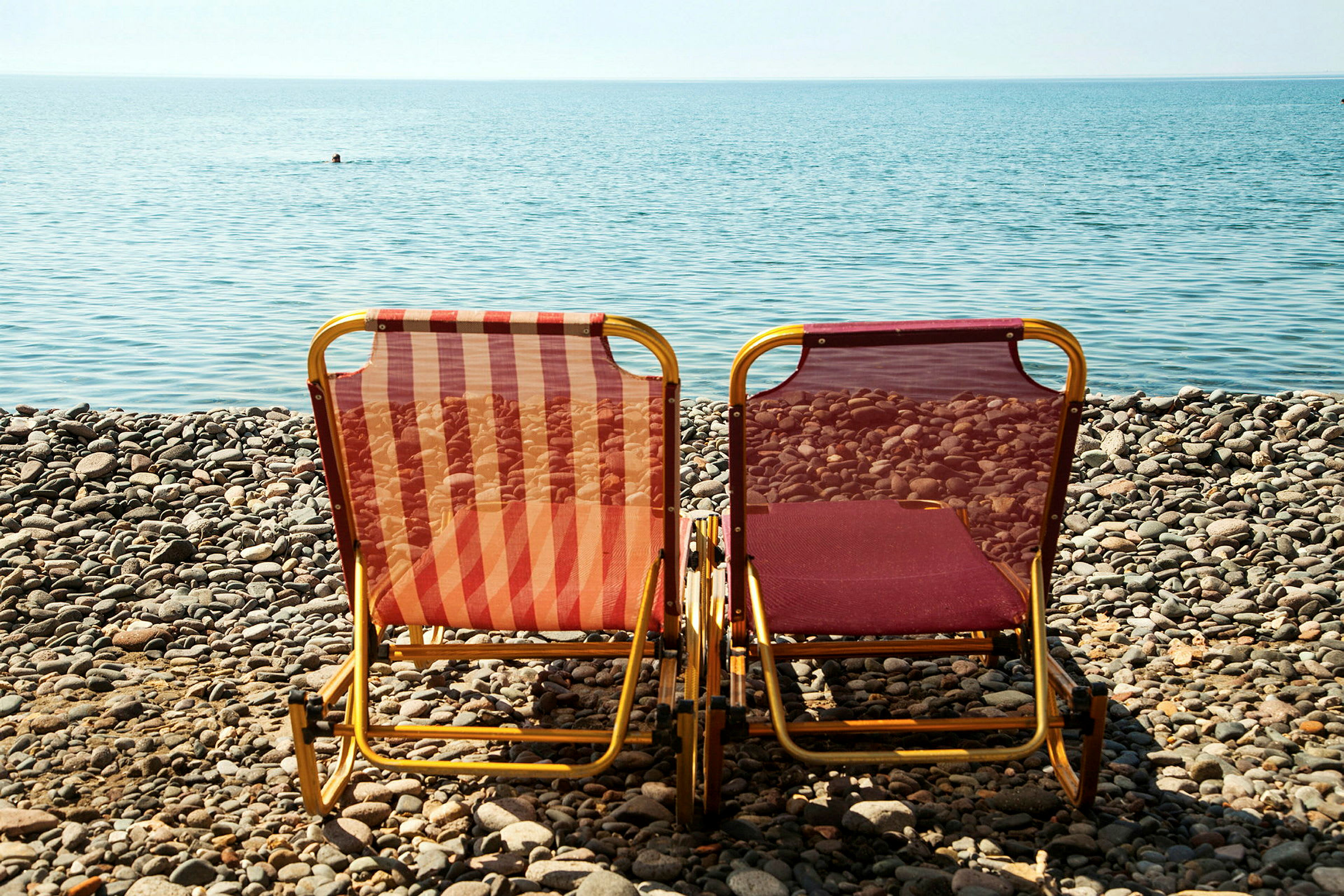 Två solstolar står på en stenig strand framför havet. (AI-genererad text)